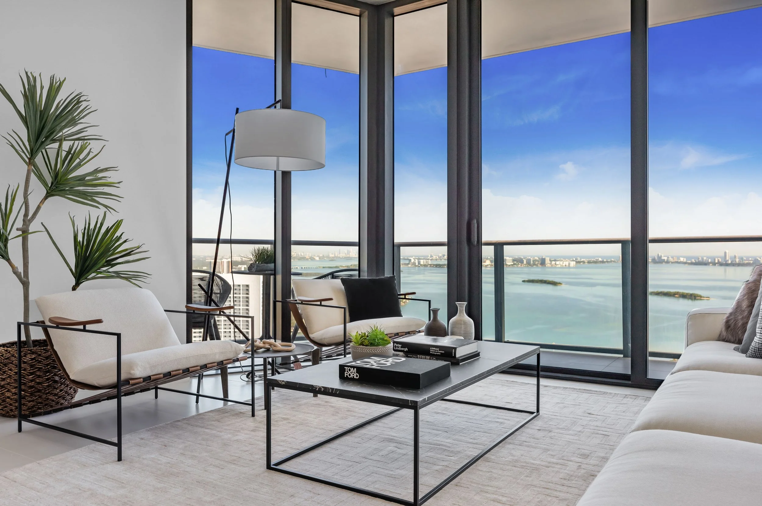 Penthouse living room with black metal-frame sling chairs, dark marble coffee table, and floor-to-ceiling Biscayne Bay views at Paraiso Bayviews in Edgewater, Interior Design by CURATED.