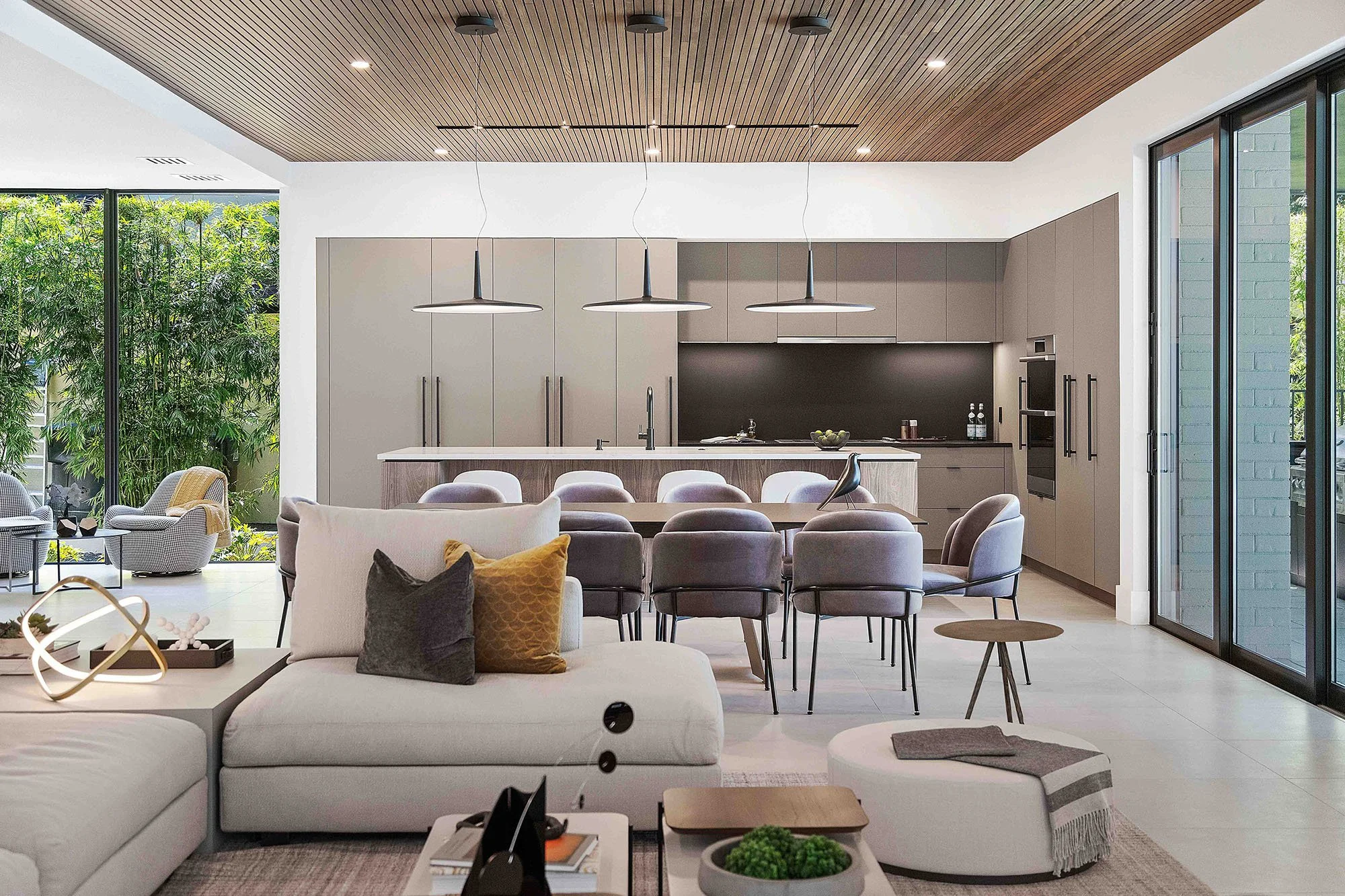 Open-concept living and dining area with slatted wood ceiling, disc pendant lights, and gray upholstered chairs on Lake Rowena, Interior Design by CURATED.