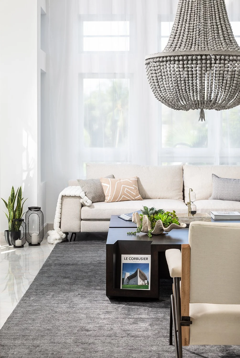 Coastal contemporary living room with cream sofa, chunky knit throw, dark wood coffee table with succulent-filled clam shell, and sheer white drapery at Aqua on Allison Island in Miami Beach, Interior Design by CURATED.