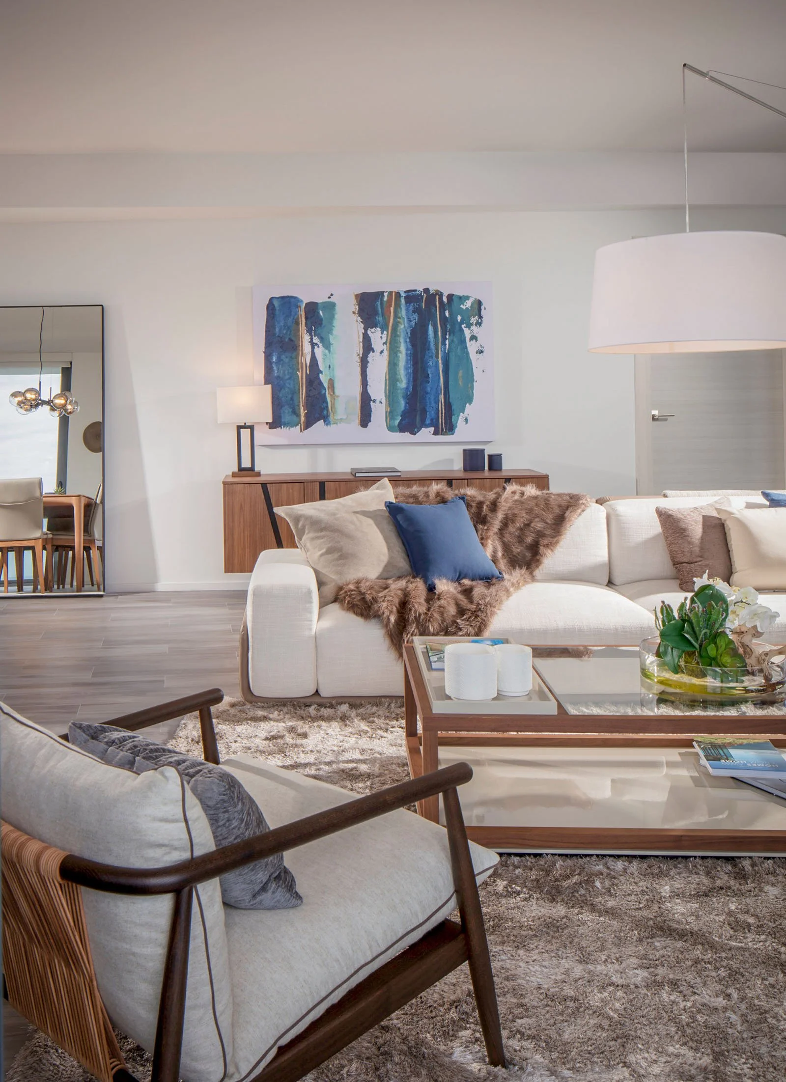 Living room with white sectional, faux fur throw, walnut and glass coffee table, and blue abstract artwork above a wood credenza in Brickell, Interior Design by CURATED.