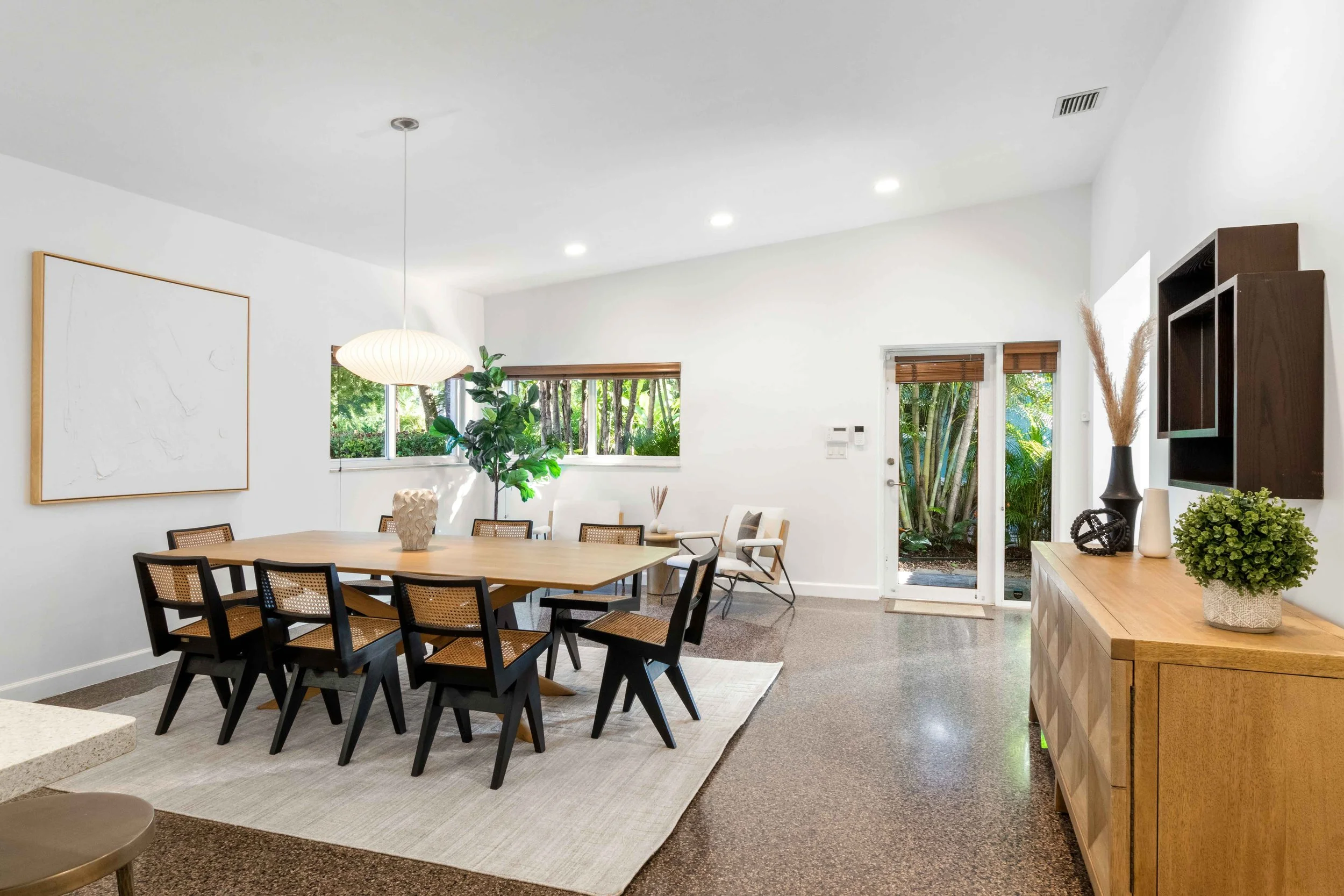 Mid-century modern dining room with black cane chairs, light wood table, paper globe pendant, and terrazzo floors in Miami Shores, Interior Design by CURATED.