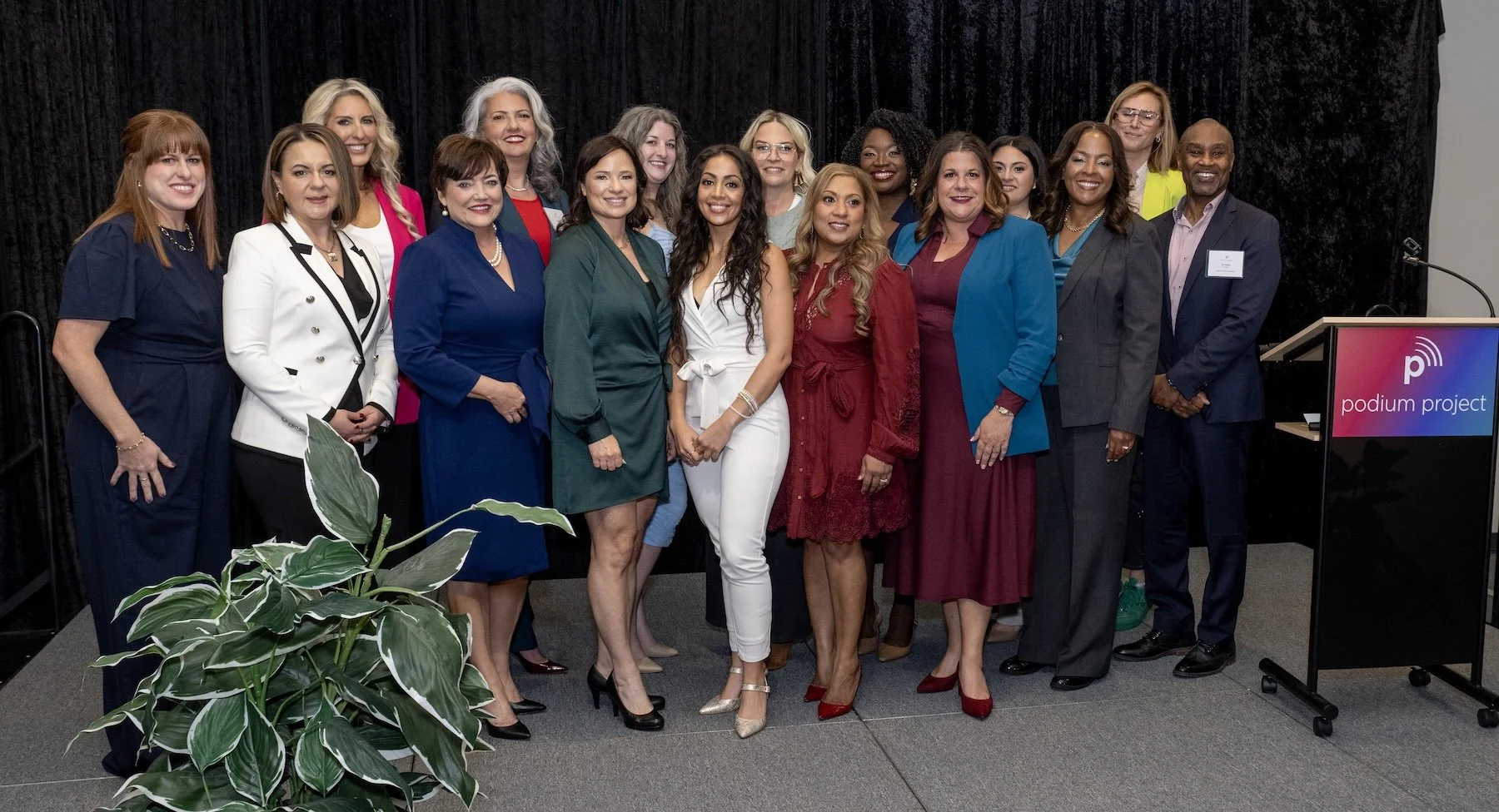 Podium Project Founders and Speakers in professional attire posing on a stage with a podium that reads "podium project".