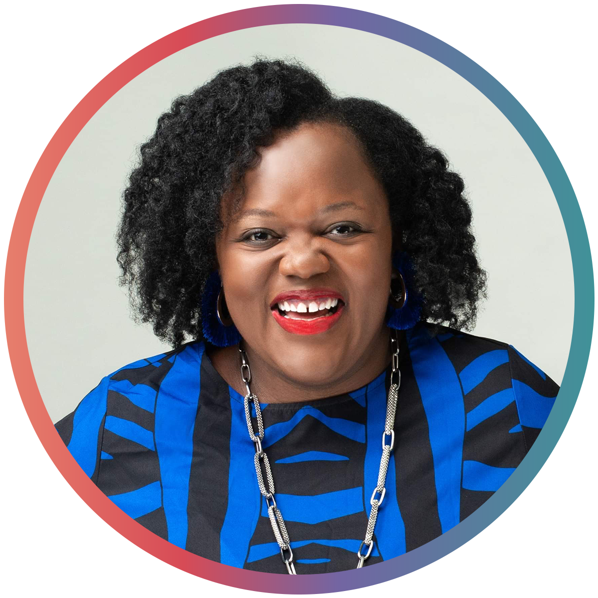 A woman smiling with braces, wearing a blue and black patterned top, blue earrings, and a long chain necklace.