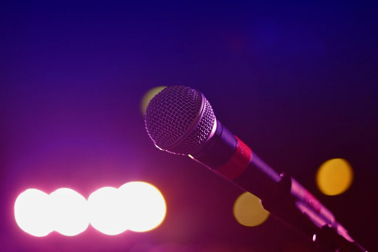 Close-up of a microphone on a stand against a dark background with colorful stage lights.
