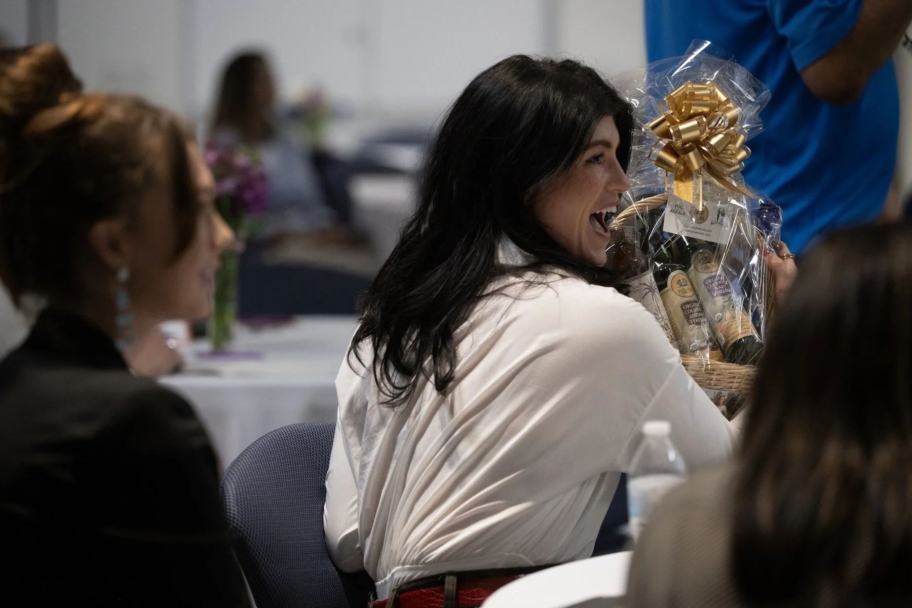 Woman laughing while holding a gift basket at a social gathering or celebration event.