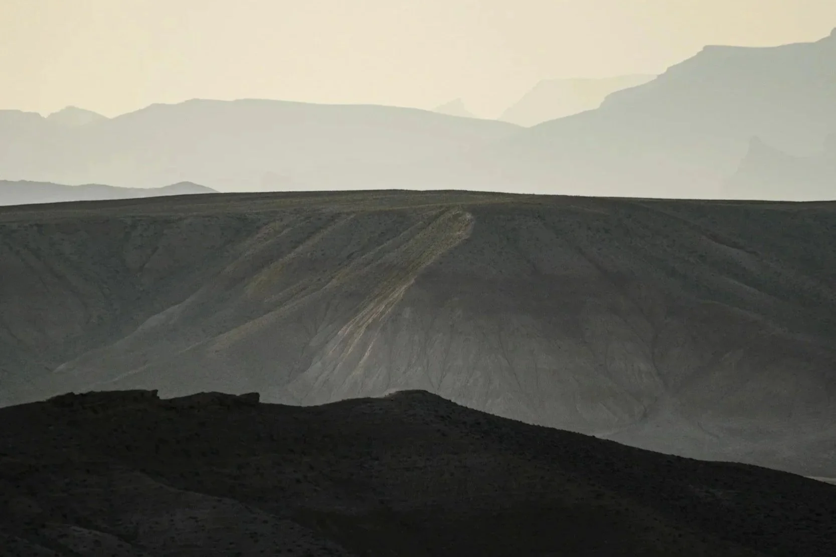 Bergige Landschaft mit mehreren Hügeln und Bergen im Hintergrund, im Abendlicht