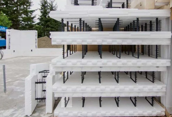 Stacked white foam and metal racks, part of a construction or storage site, with a house in the background.