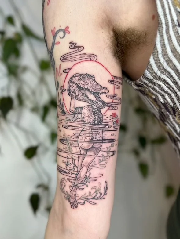 Tattoo of a crocodile with a human body, standing in water with a sunset or full moon in the background, and decorative plant elements surrounding the scene.