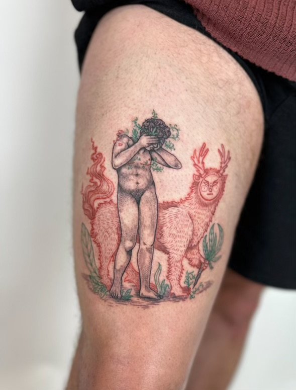 Tattoo of a classical-style nude transmasc figure with curly hair covering his face, standing in front of a stylized deer with antlers, surrounded by green foliage on a person's thigh.