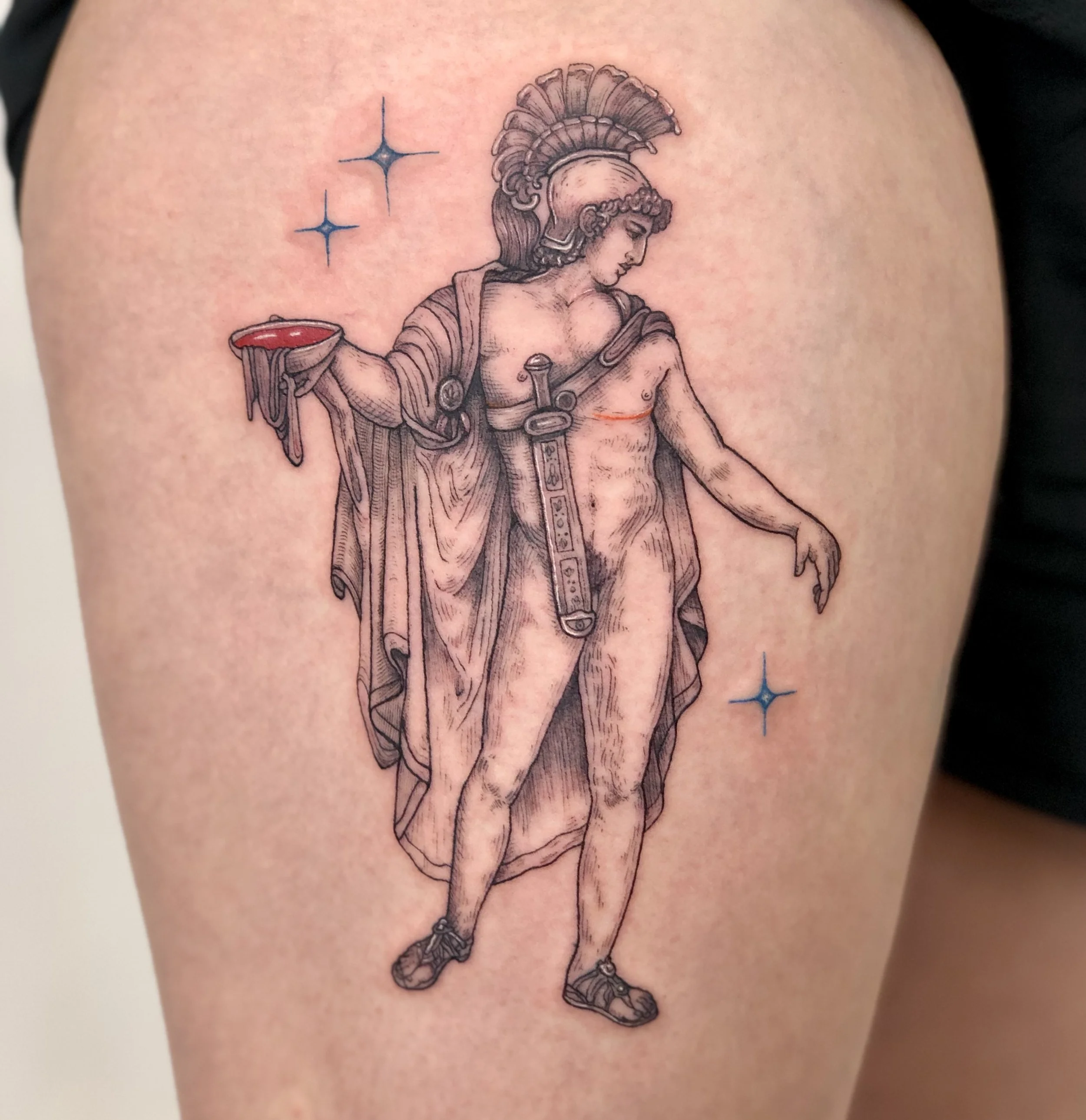 Tattoo of a transmasculine classical statue of a male warrior with a helmet, armor, and a sword, holding a red bowl, surrounded by four blue stars.