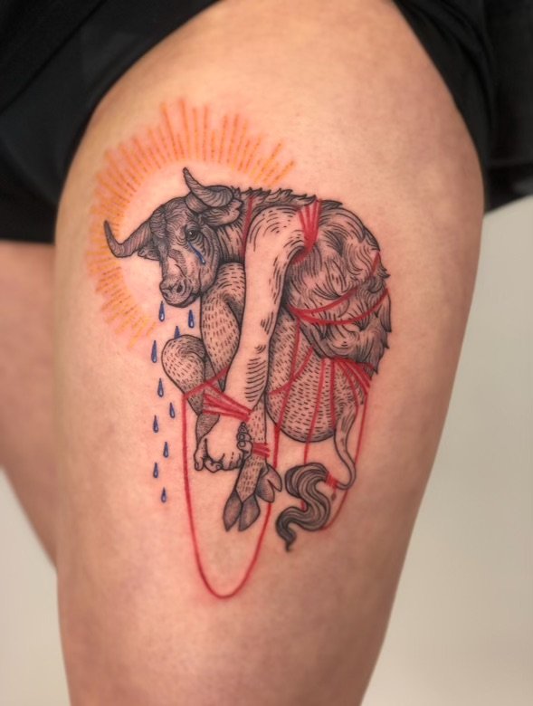 A tattoo of a crying unicorn with a sun behind its head, featuring red and black lines, watercolor elements, and blue tears.