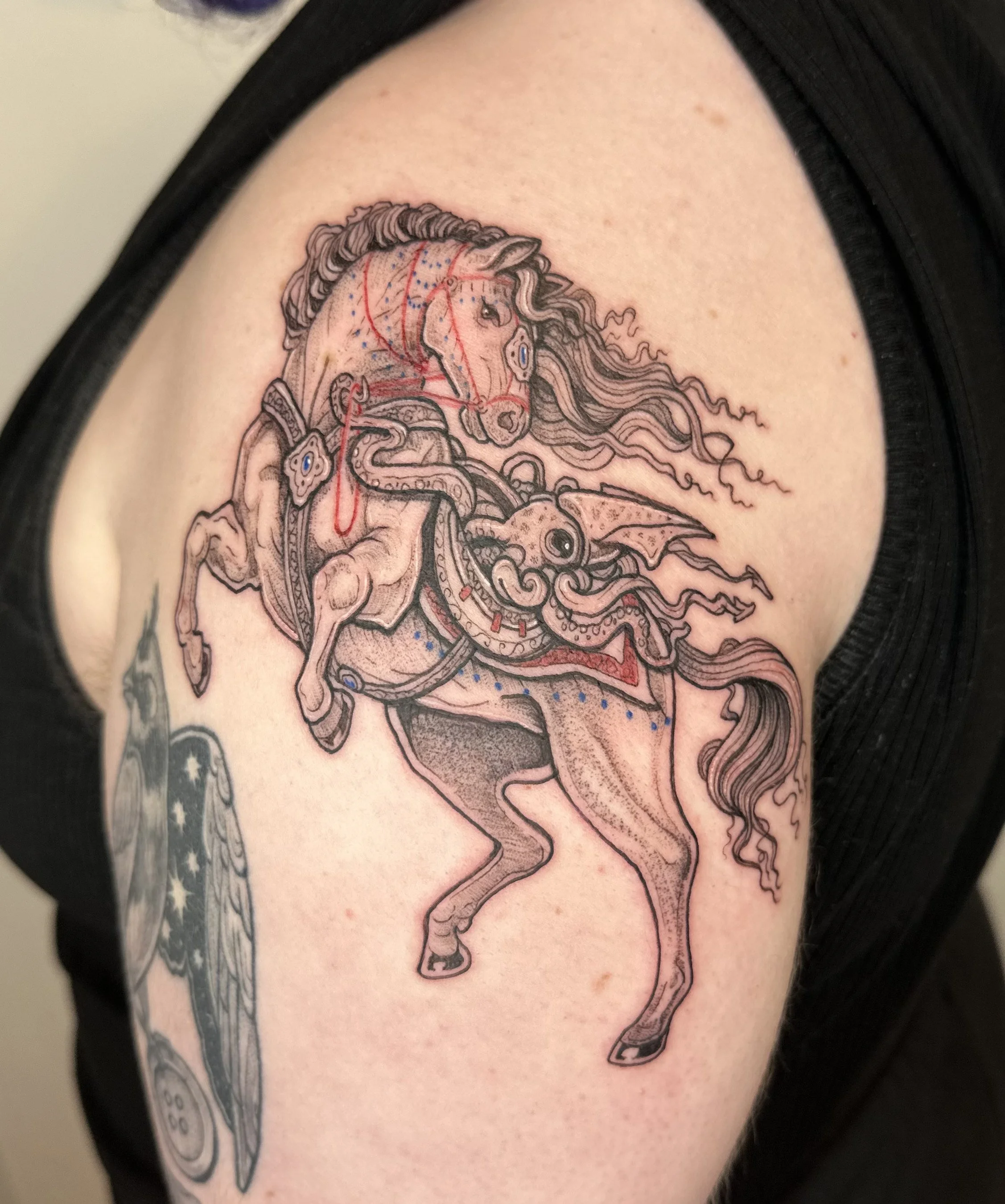 Tattoo of a detailed, artistic depiction of a rearing horse with flowing mane, and a squid in its saddle bag on a person's upper arm.