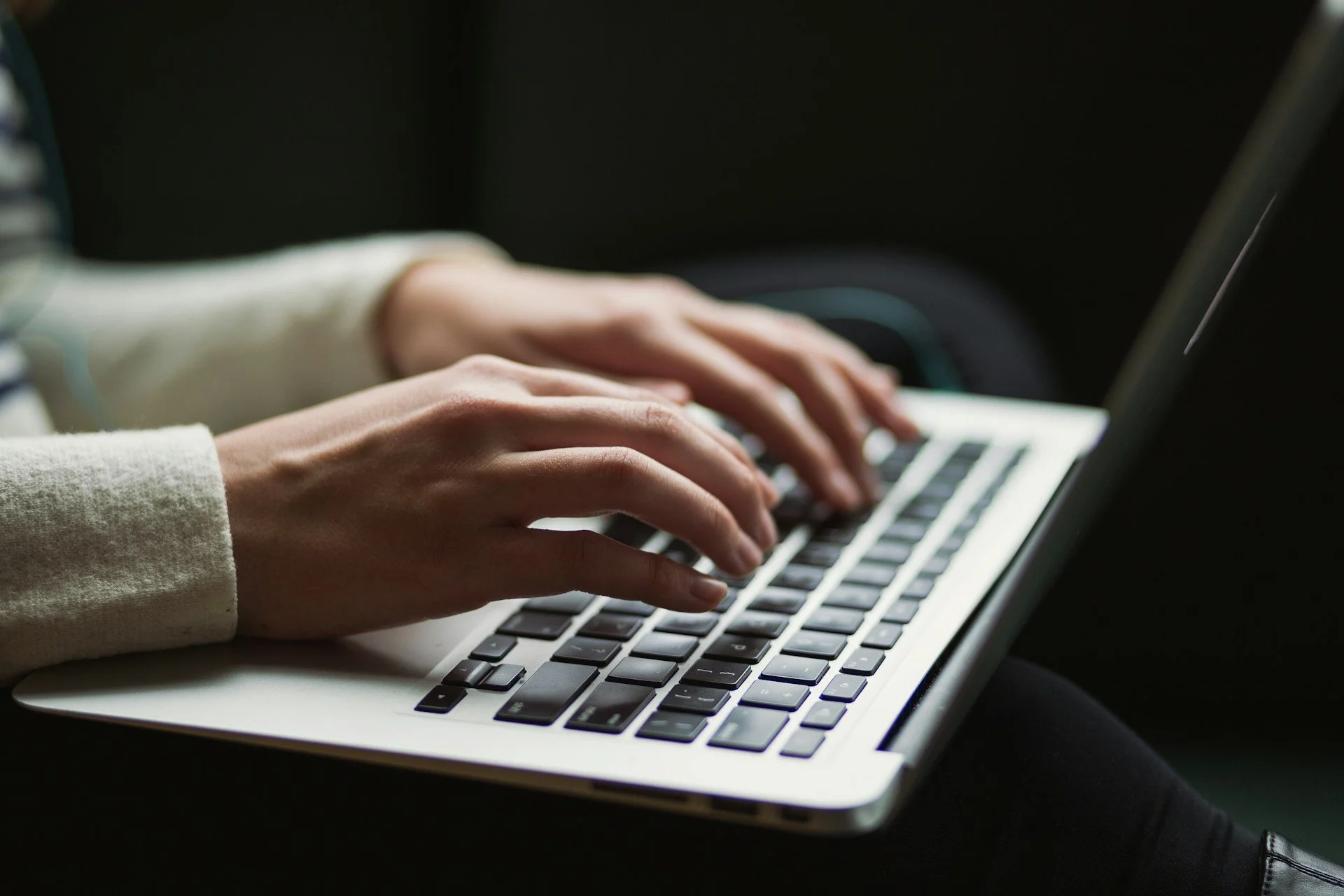 Person typing on a laptop keyboard in a dark setting.