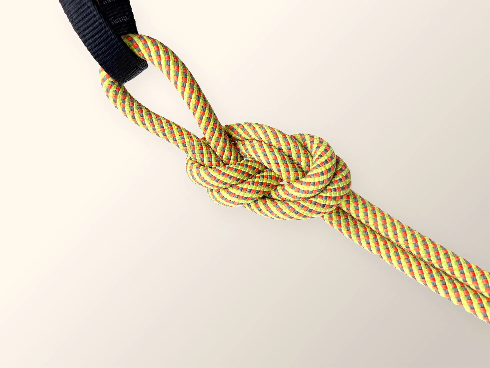 Colorful climbing rope tied in a knot with a black strap on a white background.