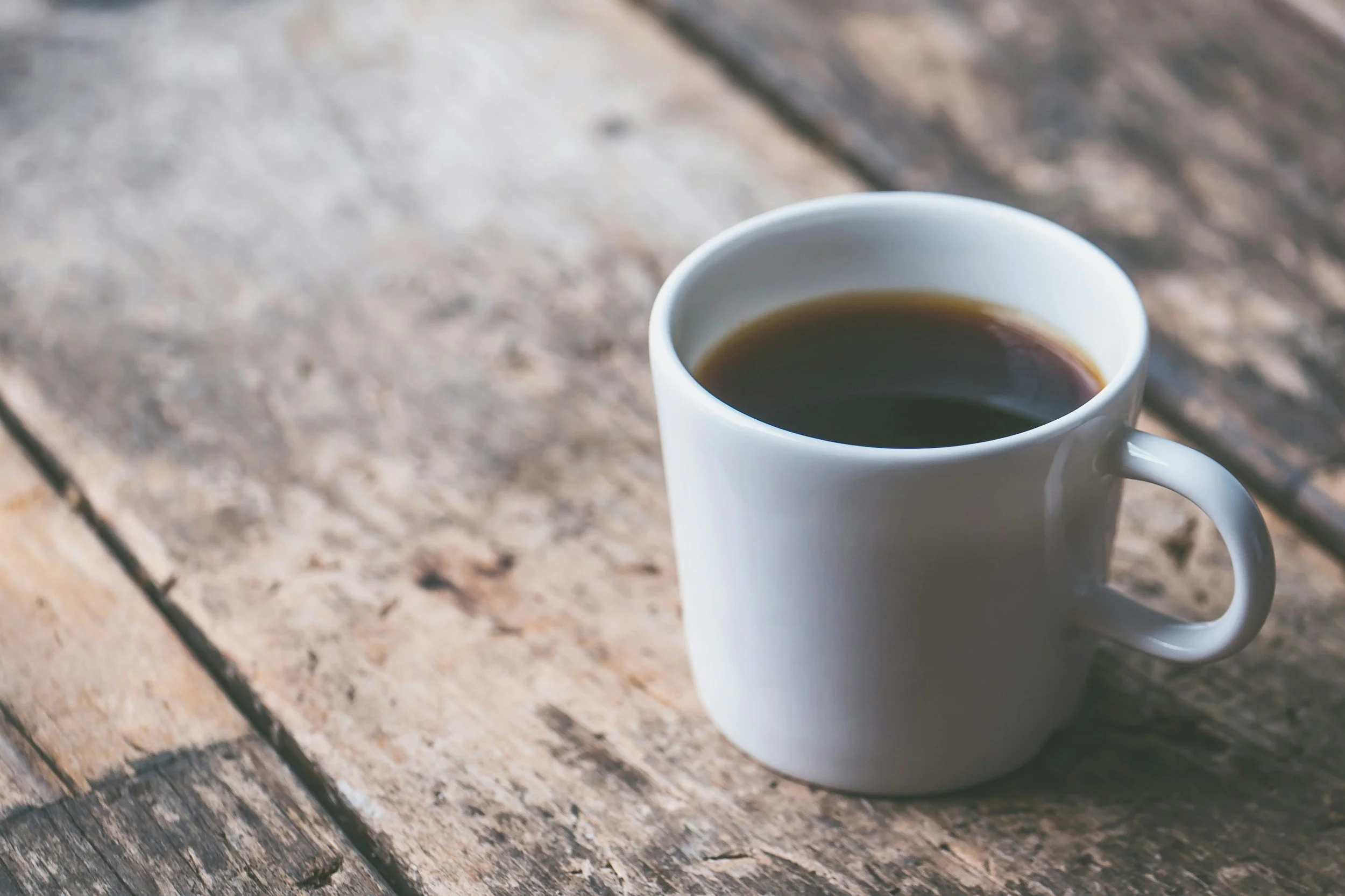 A white ceramic mug filled with black coffee on a rustic wooden table.