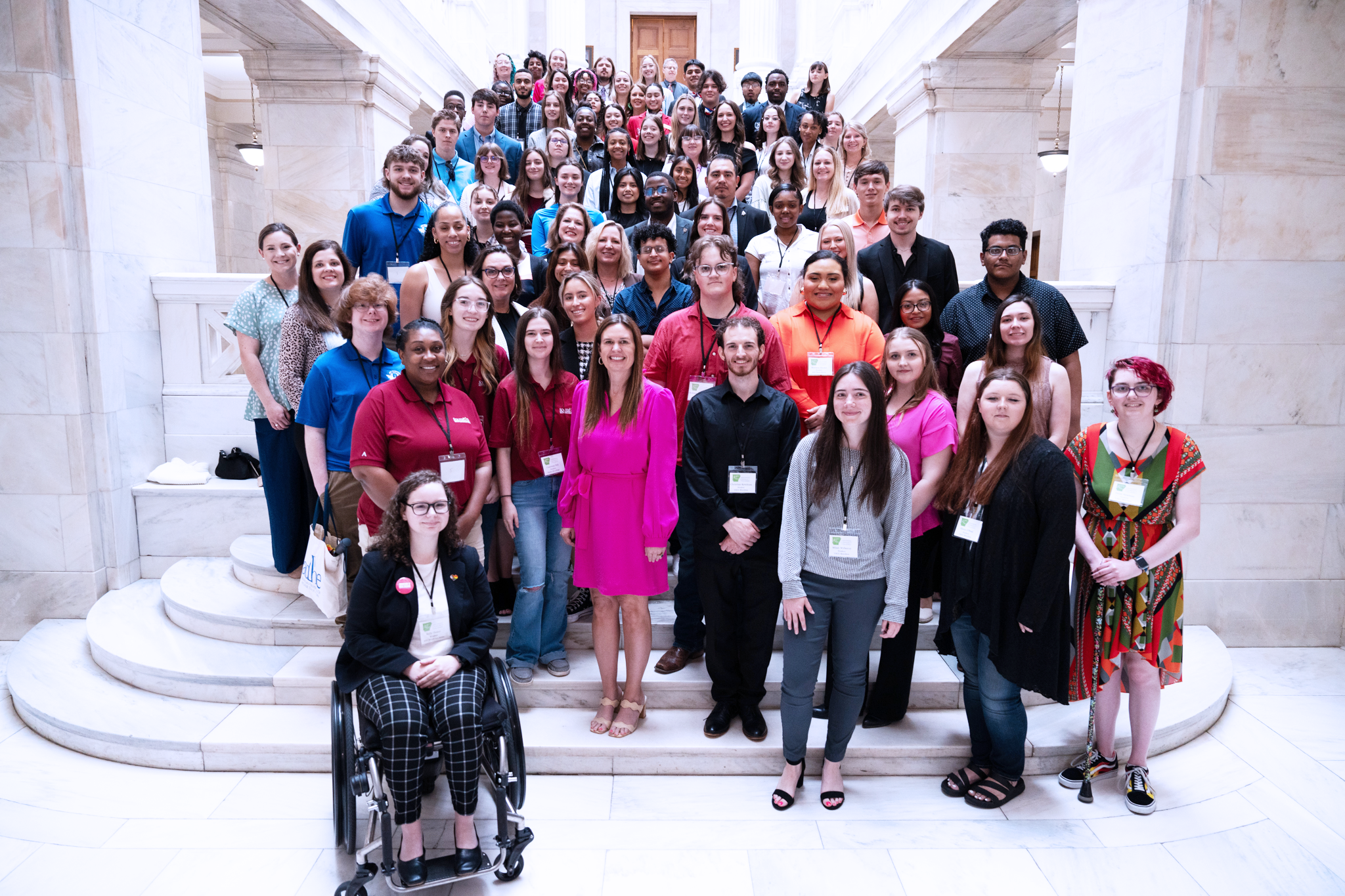 Arkansas community college student leaders posing with Governor Sarah Huckabee Sanders on the marble steps within the Arkansas State Capitol building.