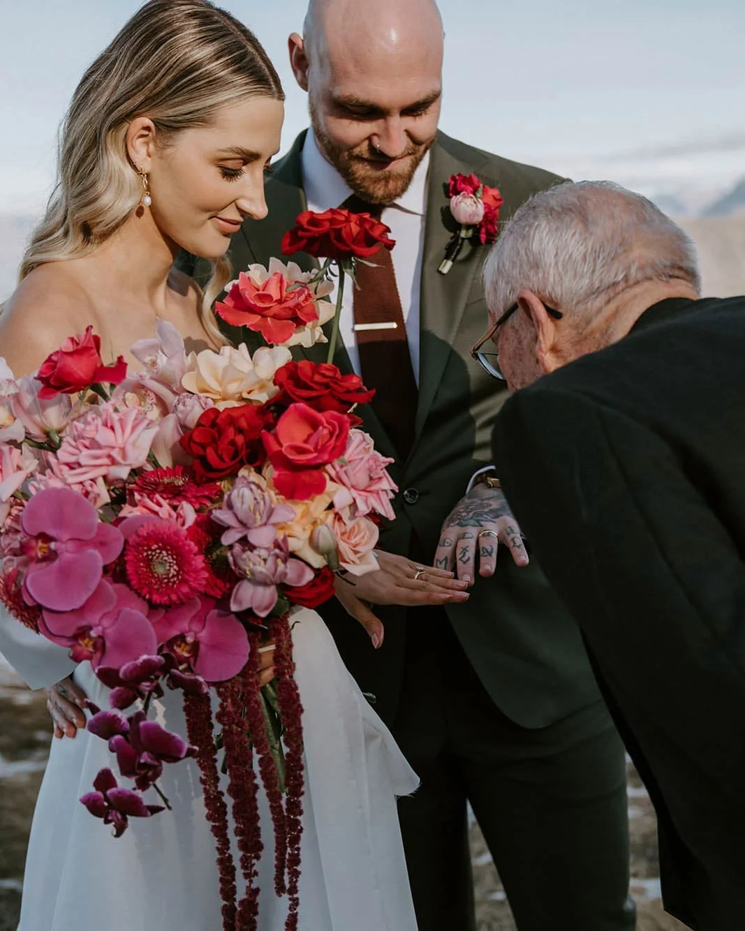 A bride holding a large bouquet of pink, red, and purple flowers.