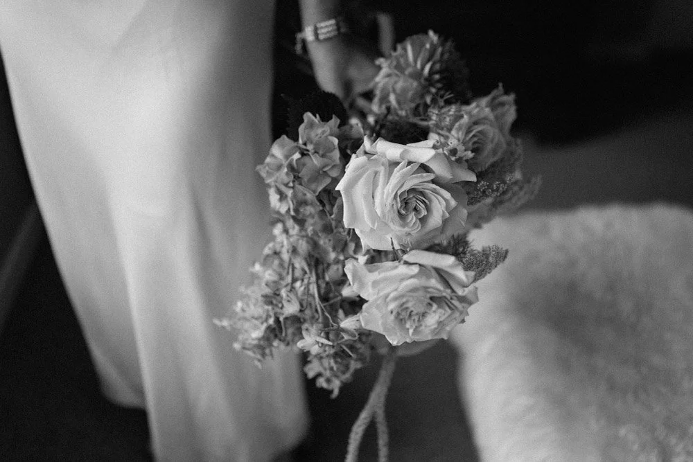 Black and white photo of a bouquet of flowers, including roses, held by a person in a light-colored garment.
