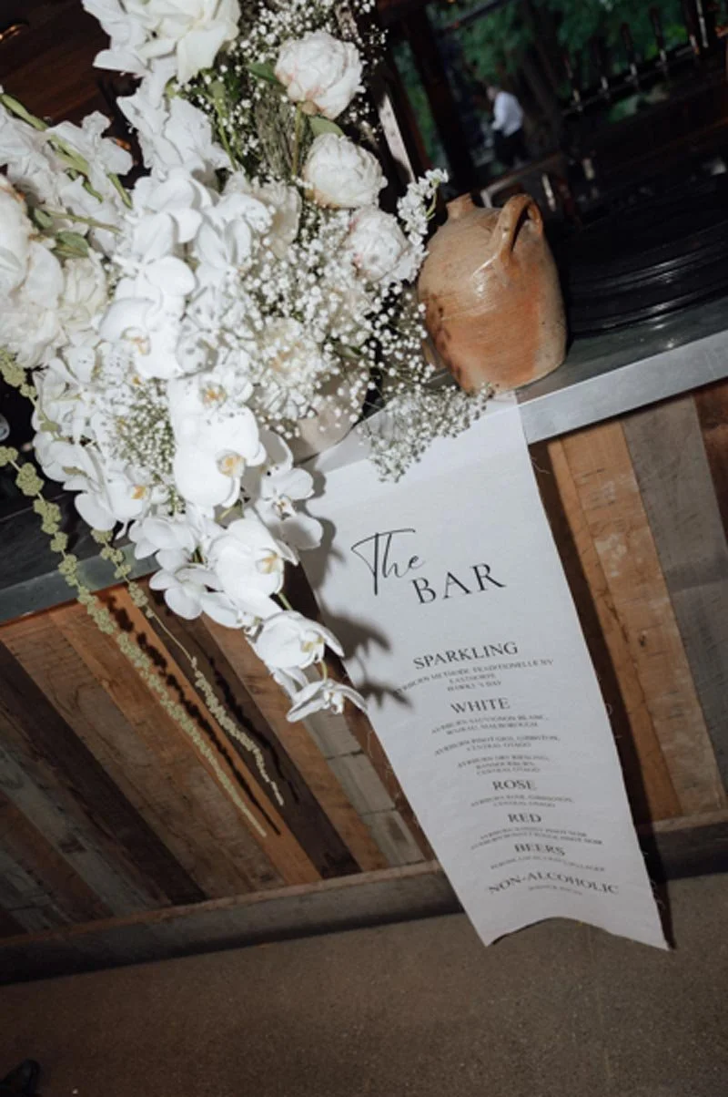 A floral arrangement with white flowers and baby's breath next to a paper sign listing bar options.