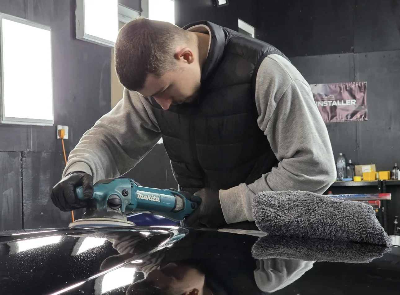 A man using a Makita electric buffer on a shiny black surface in a workshop.