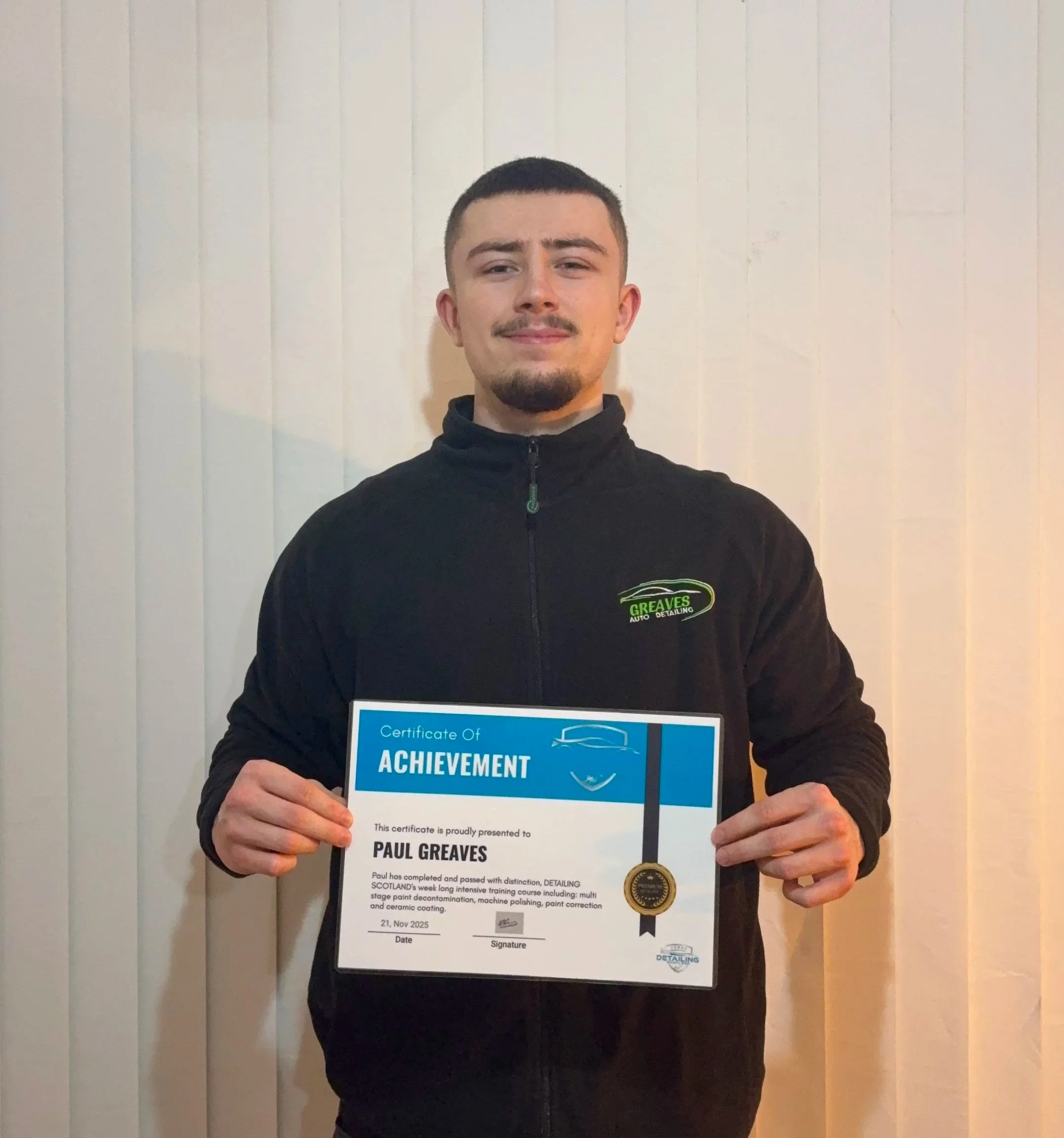 A young man holding a certificate of achievement in front of a white wall.