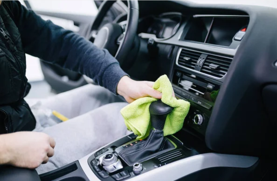 Person cleaning the dashboard of a car with a yellow cloth.