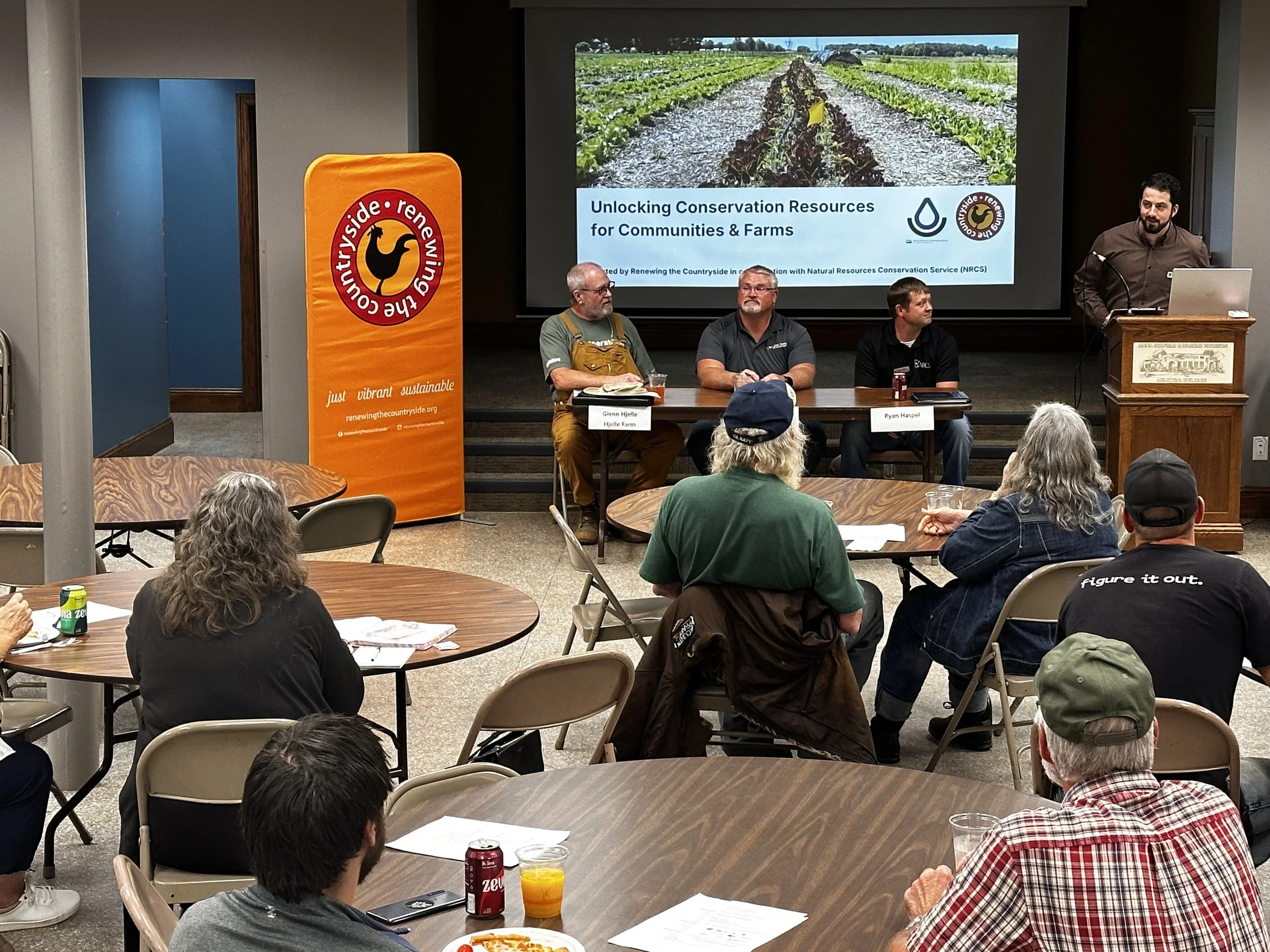 A conservation coordinator and panelists give a presentation to farmers and community members at an event