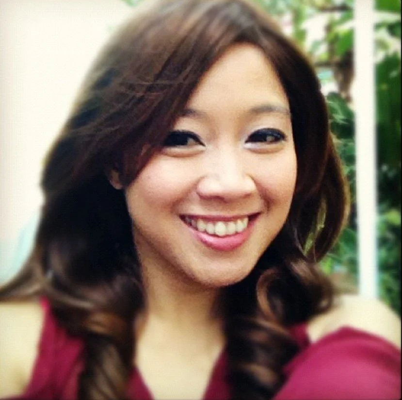 A woman with long brown hair smiling outdoors.