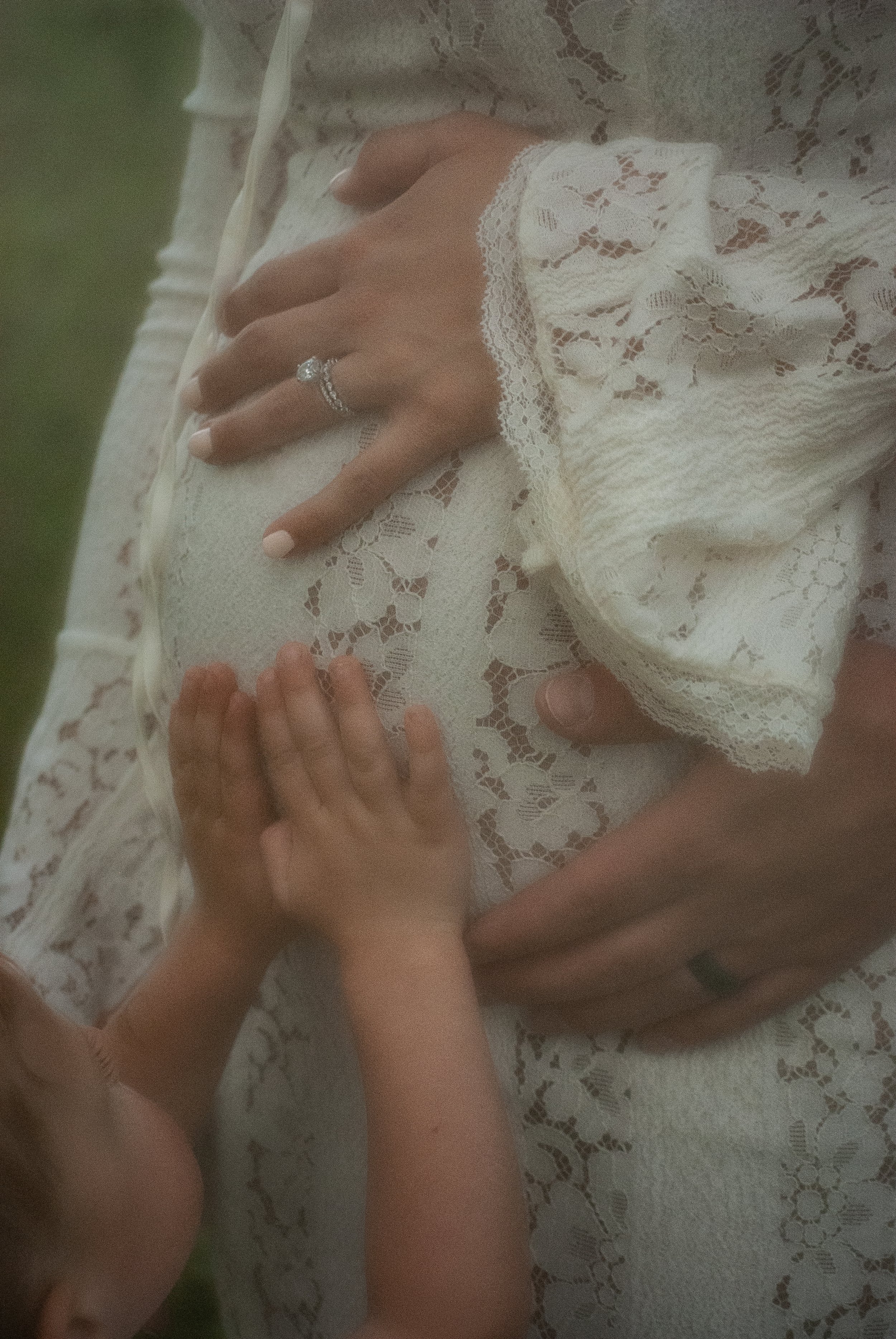 A woman in a lace dress with a ring on her finger is holding hands with a young girl, possibly a child, who is also wearing a lace dress. They are touching or holding each other's hands on a lace fabric surface.