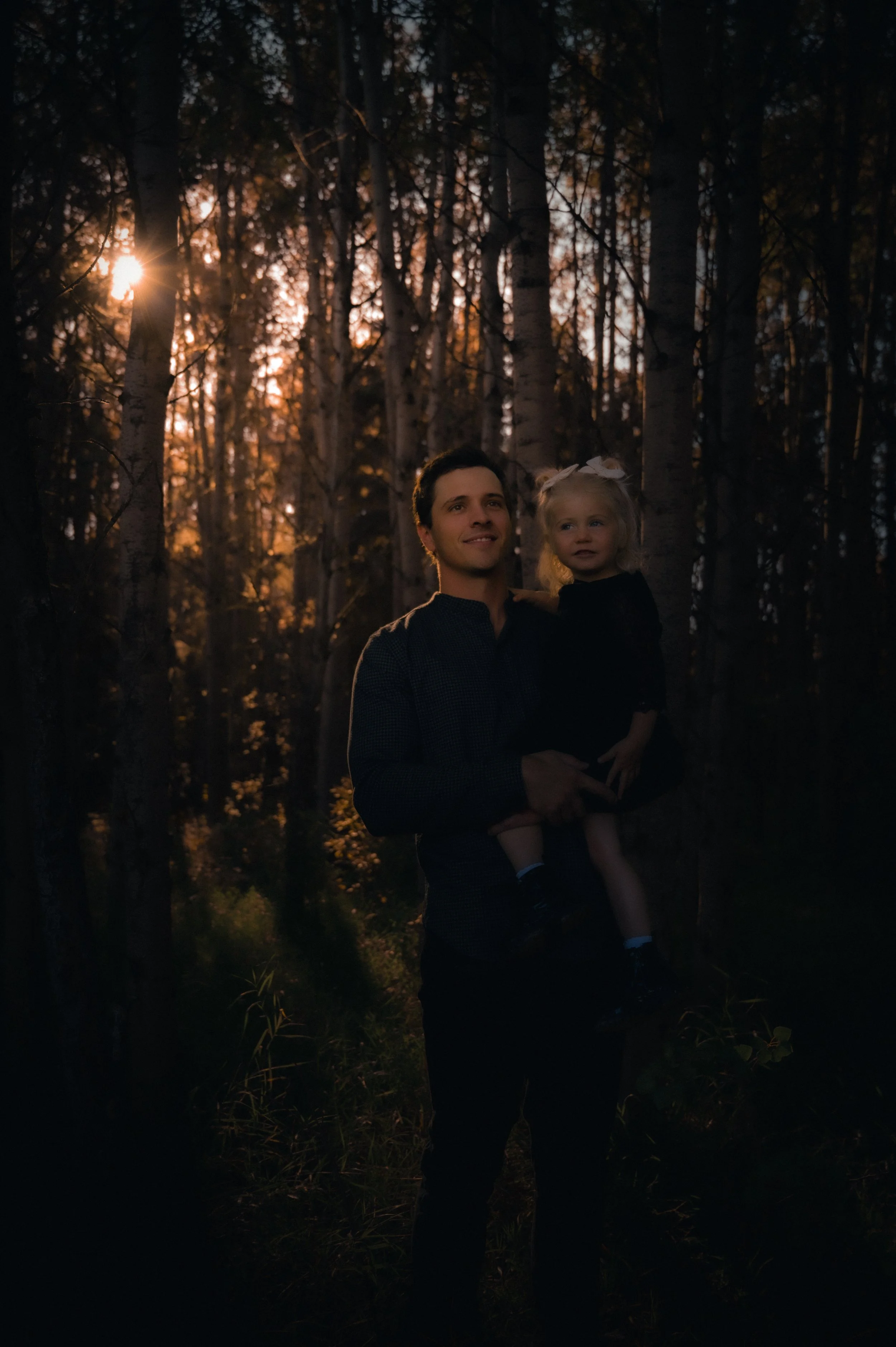 A man holding a young girl in a forest during sunset.