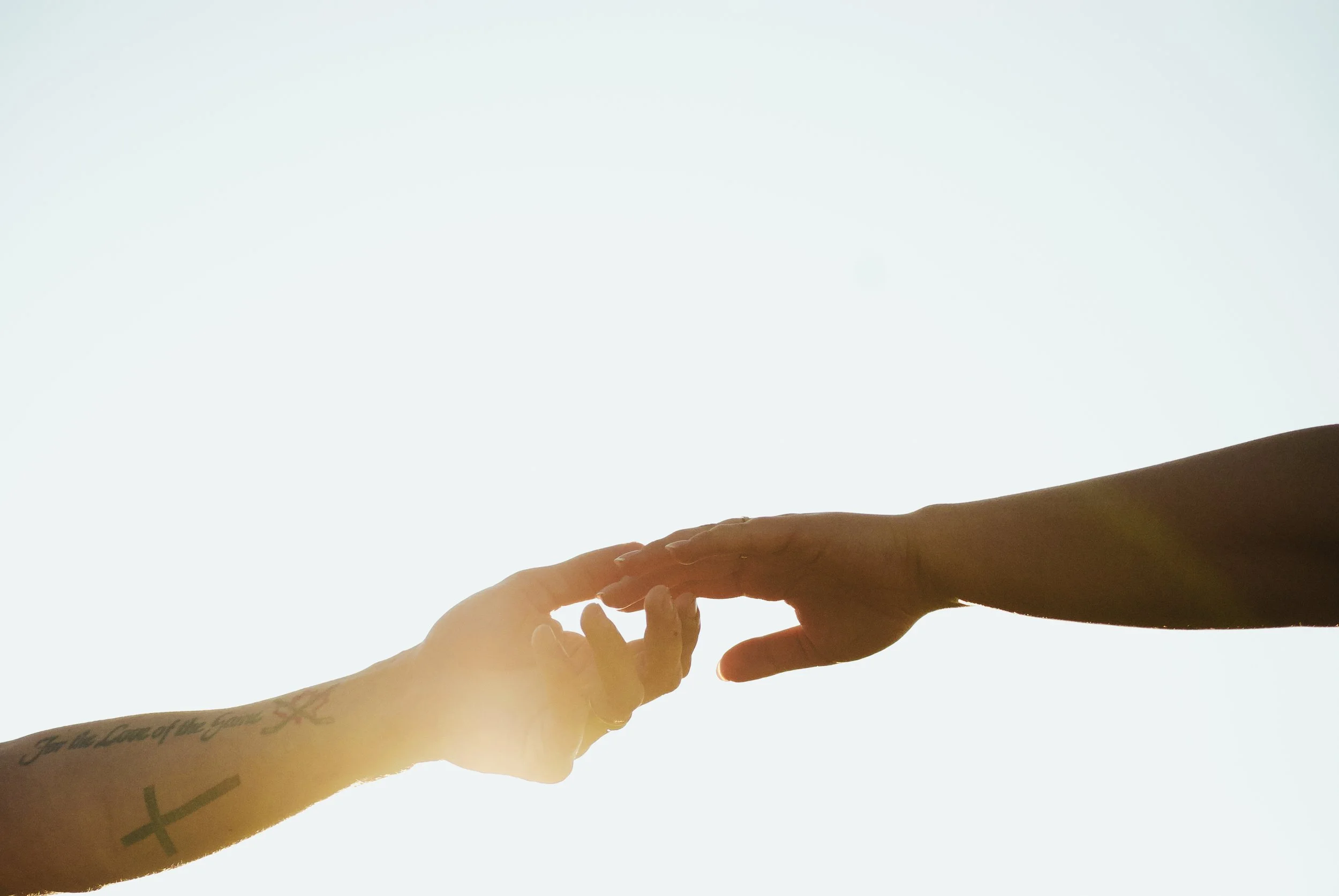 Two hands reaching out to touch fingers against a bright sky background.