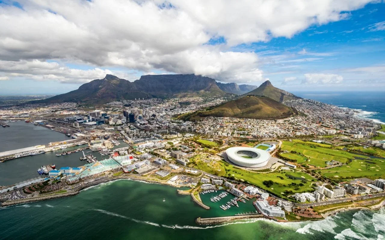 Aerial view of Cape Town, South Africa, featuring Table Mountain, Lion's Head, the cityscape, V&A Waterfront, and the Atlantic Ocean.