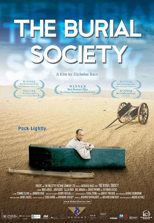 Movie poster for 'The Burial Society' featuring a man sitting on a makeshift boat in a desert with an old wooden cart and wagon wheel in the background. The poster includes film awards and critic reviews.
