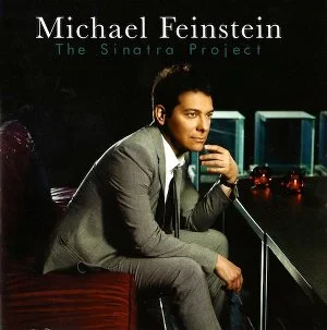 Book cover titled 'Michael Feinstein The Sinatra Project' featuring a young man in a gray suit sitting at a bar, holding a microphone, with a dark background and illuminated objects.