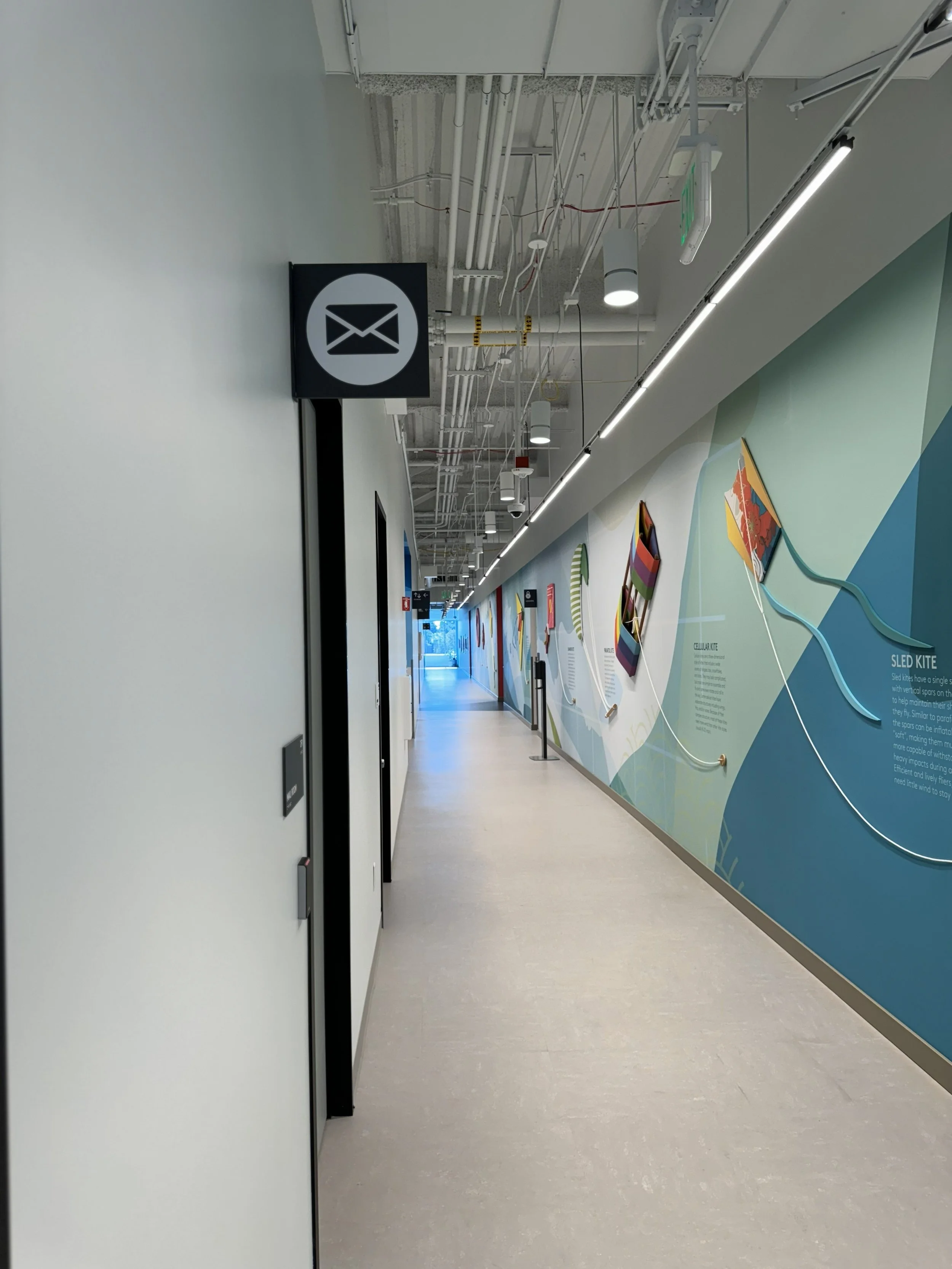 Office corridor with hanging wayfinding signage and large-scale environmental wall graphics installed for corporate workplace navigation and branding.