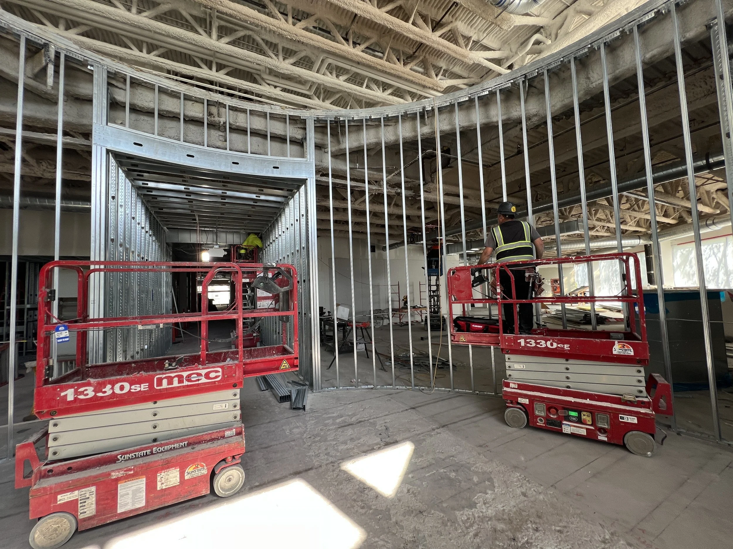 Commercial lobby under construction showing metal stud framing and lift installation during interior build-out renovation.