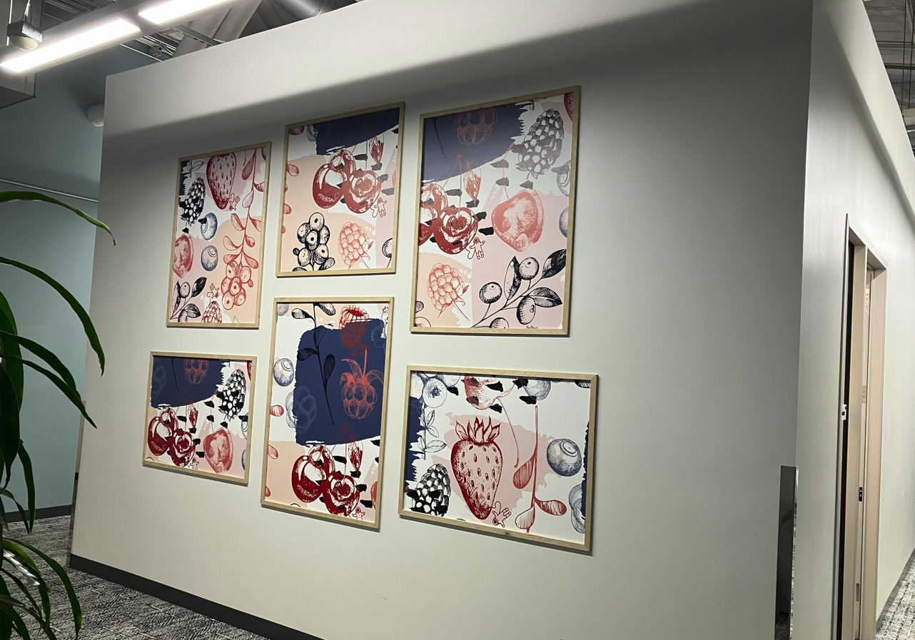 Framed environmental graphic panels featuring fruit and botanical illustrations installed on a hallway wall in an amphitheatre workspace.