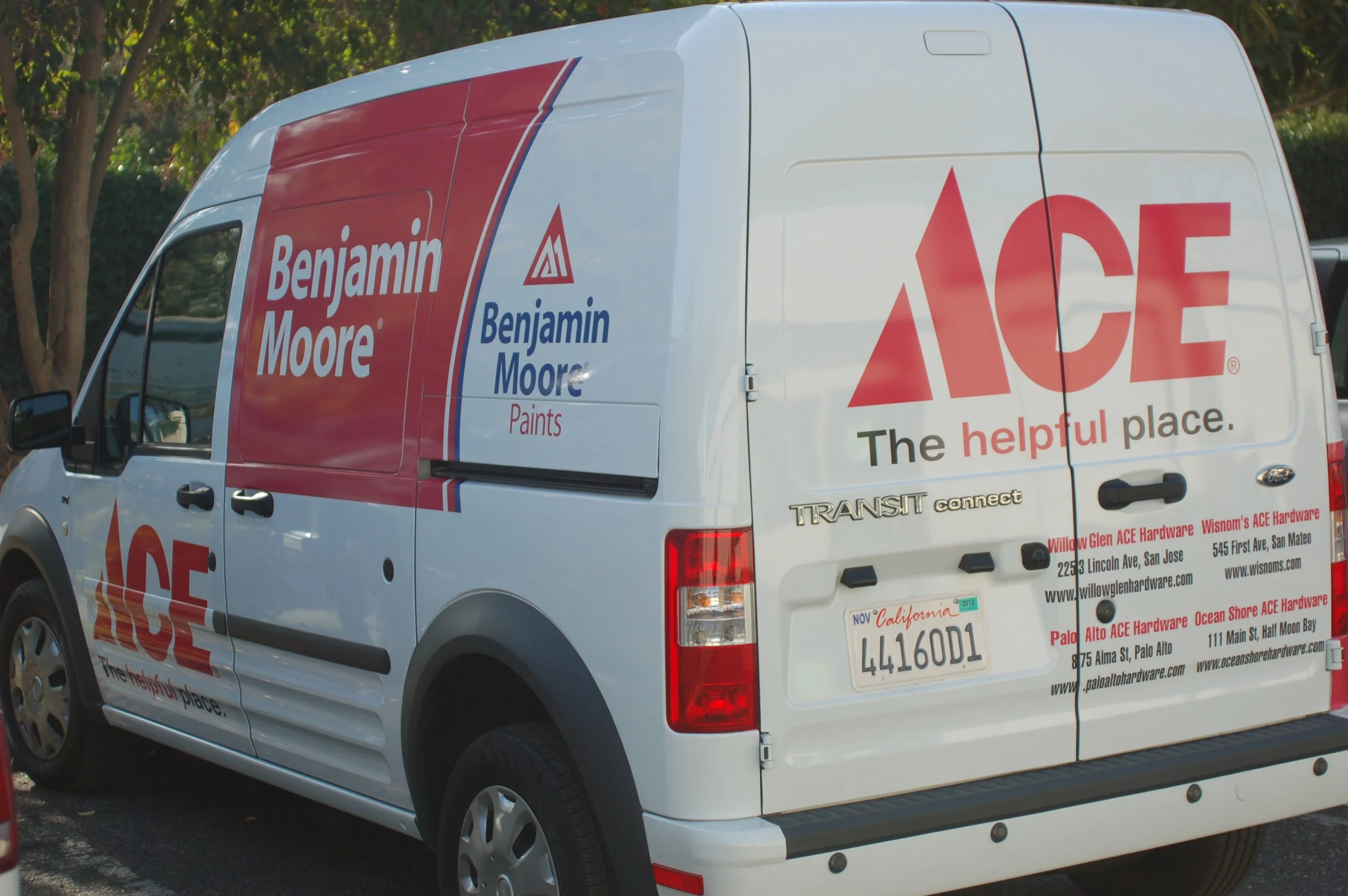 Partial commercial vehicle wrap with custom logo, lettering, and contact information applied to a white service van for business branding.