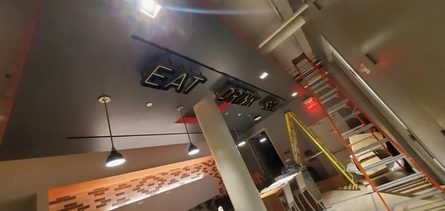 Installed dimensional “Eat Drink Sell” ceiling signage at eBay New York office featuring backlit channel letters as part of workplace environmental graphics