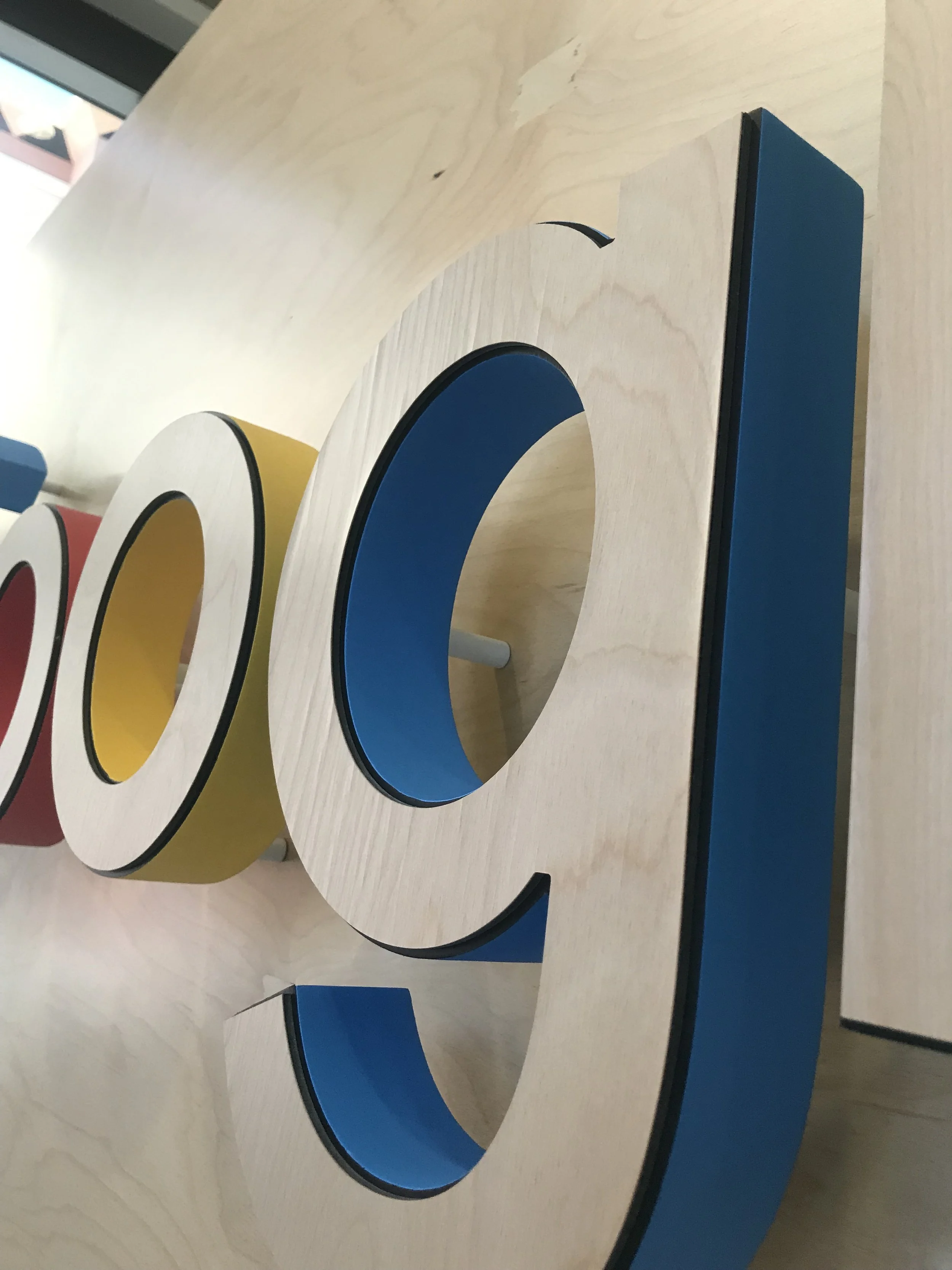 Side angle detail of dimensional Google lettering featuring birch wood veneer faces and colored acrylic returns, highlighting depth, craftsmanship, and layered construction.