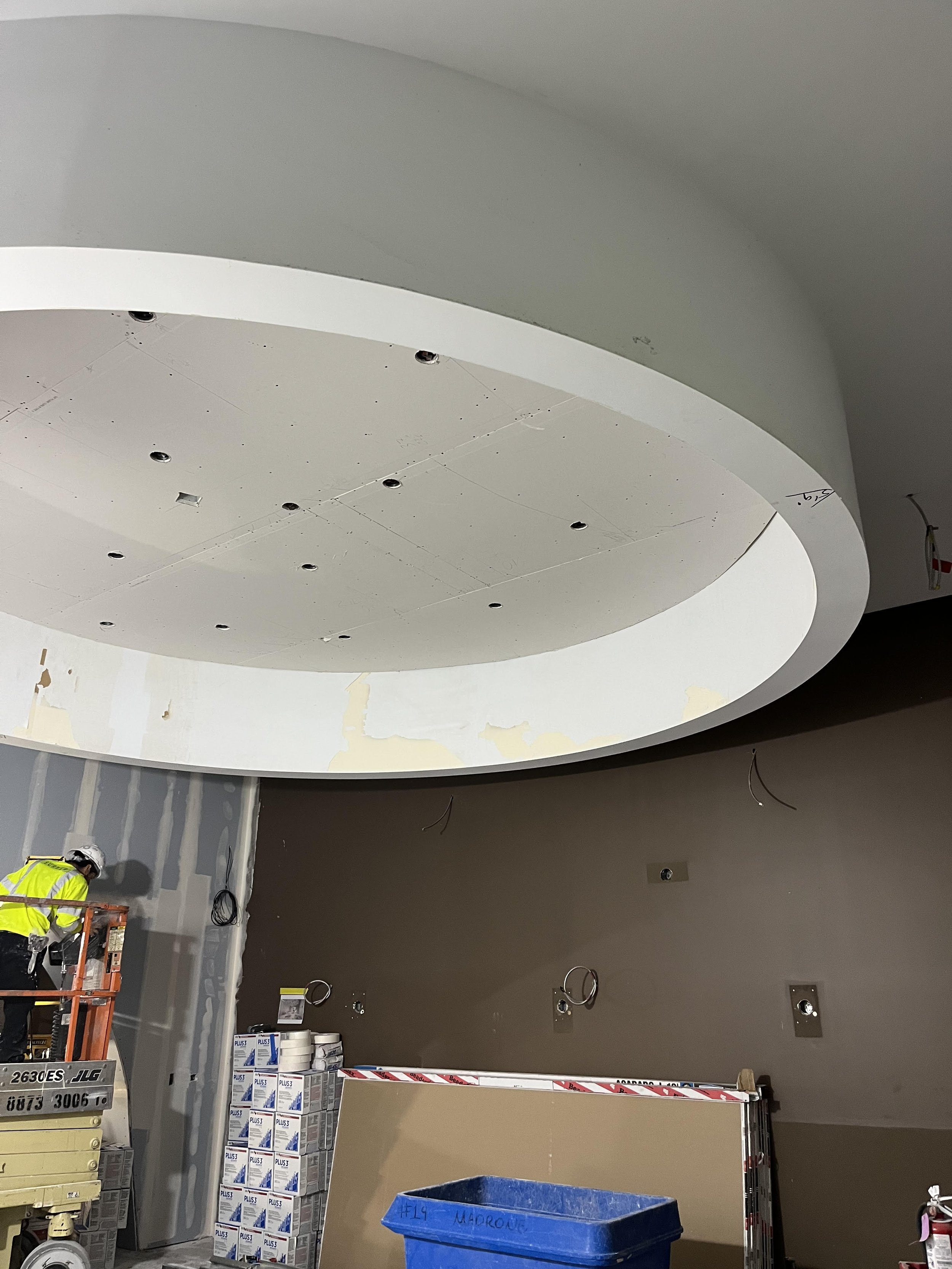 Curved drywall soffit and ceiling feature under construction with recessed lighting cutouts, joint finishing, and surface preparation for a custom commercial interior installation.