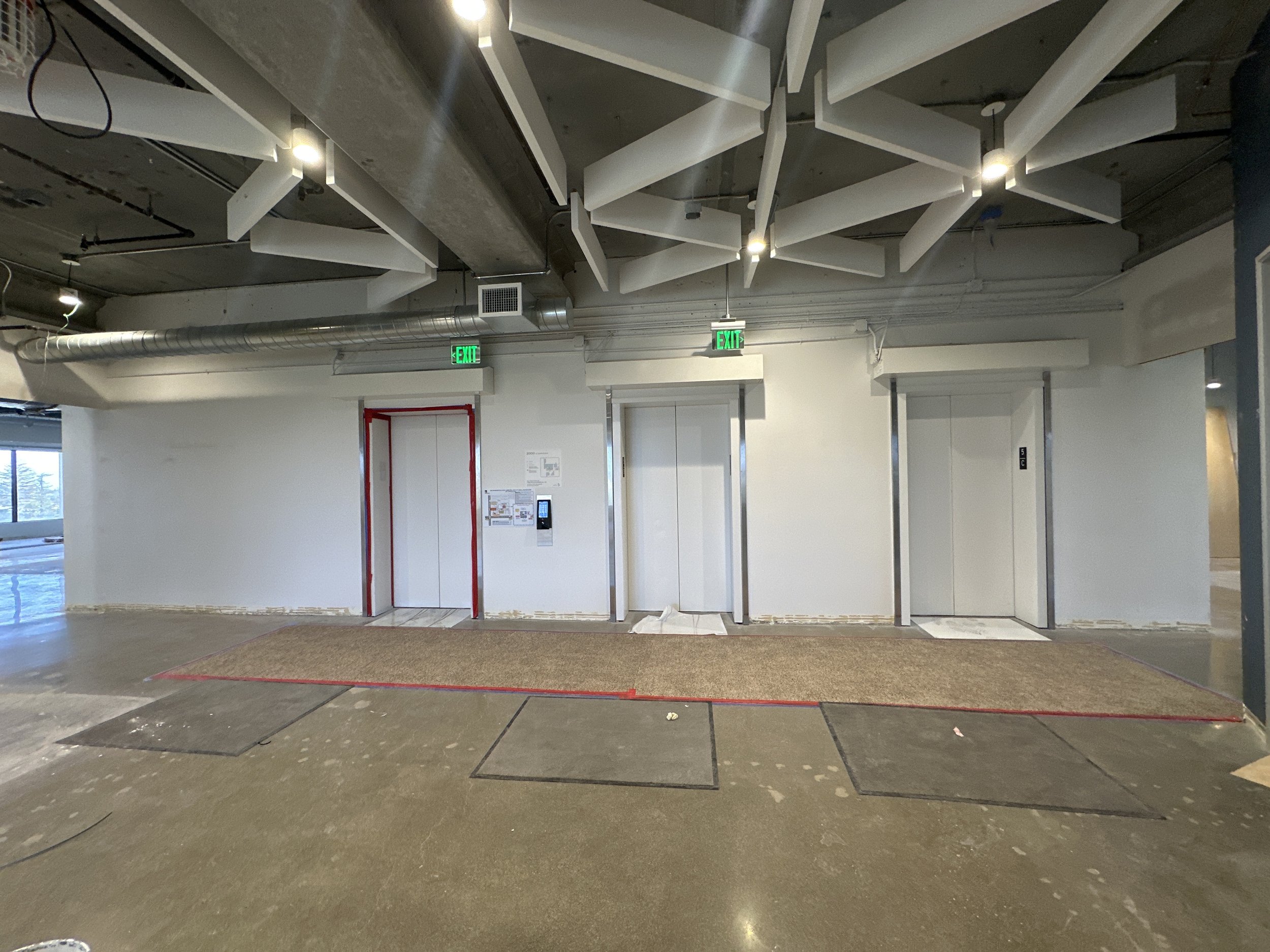 Commercial elevator lobby shown before wallcovering and environmental graphics installation, with exposed walls and construction preparation.