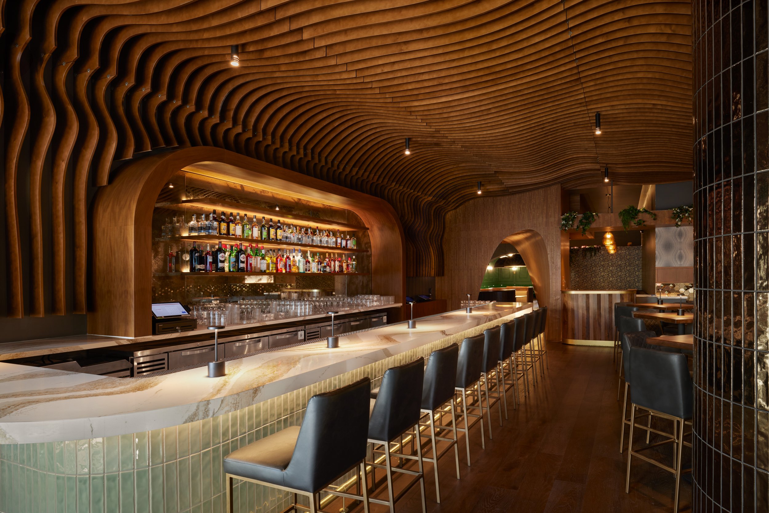 Custom curved wood millwork, architectural ceiling feature, and decorative wall finishes in modern restaurant bar interior installation.