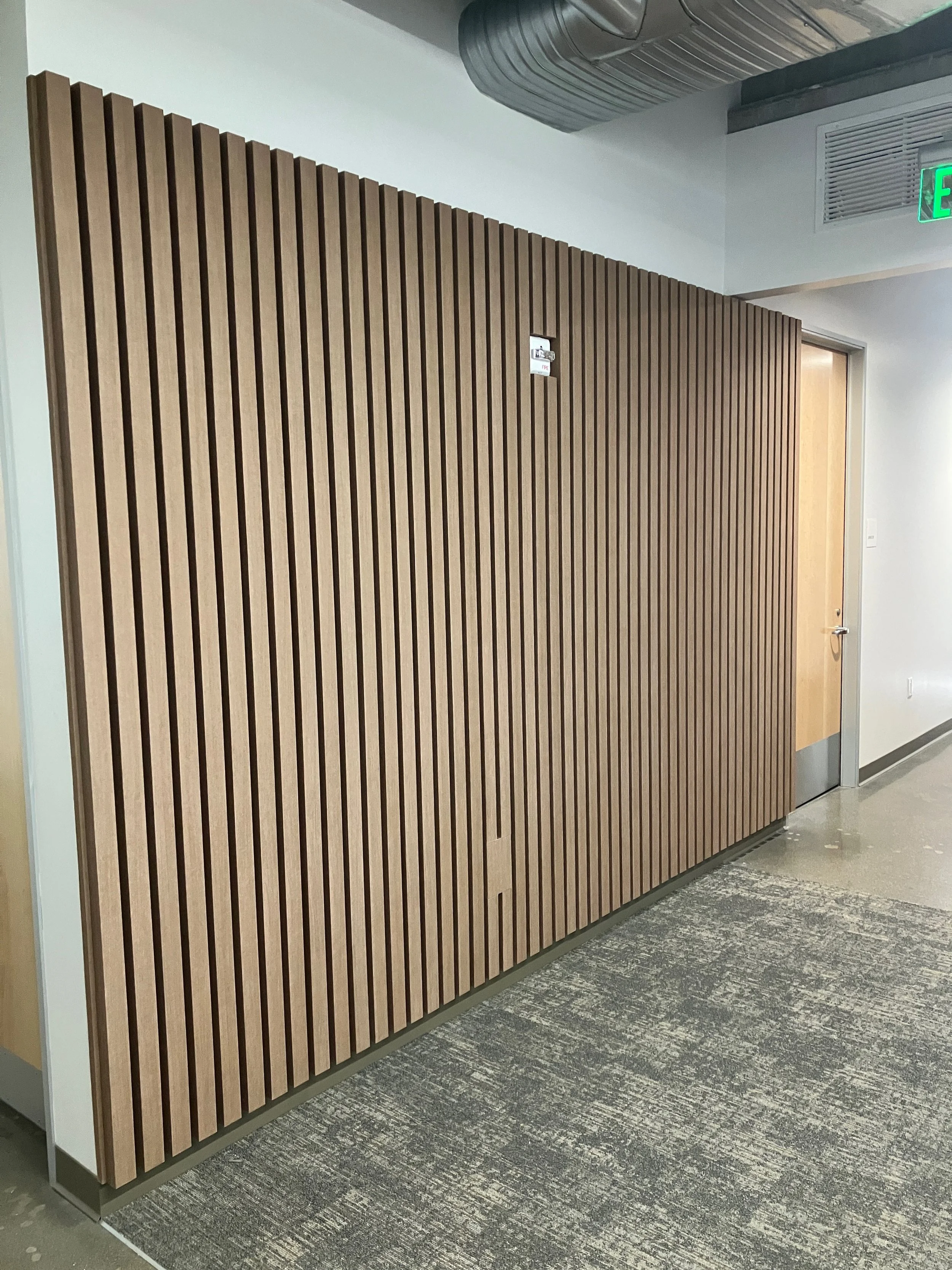 Arete wood slat acoustic wall panels installed in a commercial corridor, providing sound absorption and modern architectural texture.