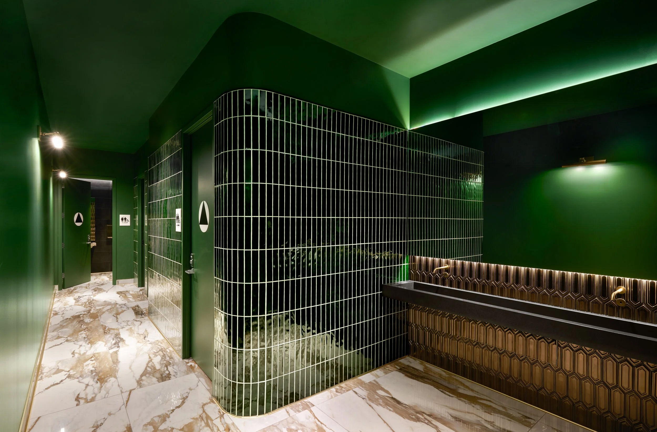 Final restroom signage installed on bathroom door, showing ADA-compliant identification with tactile lettering, Braille, and accessibility symbols in a commercial interior.