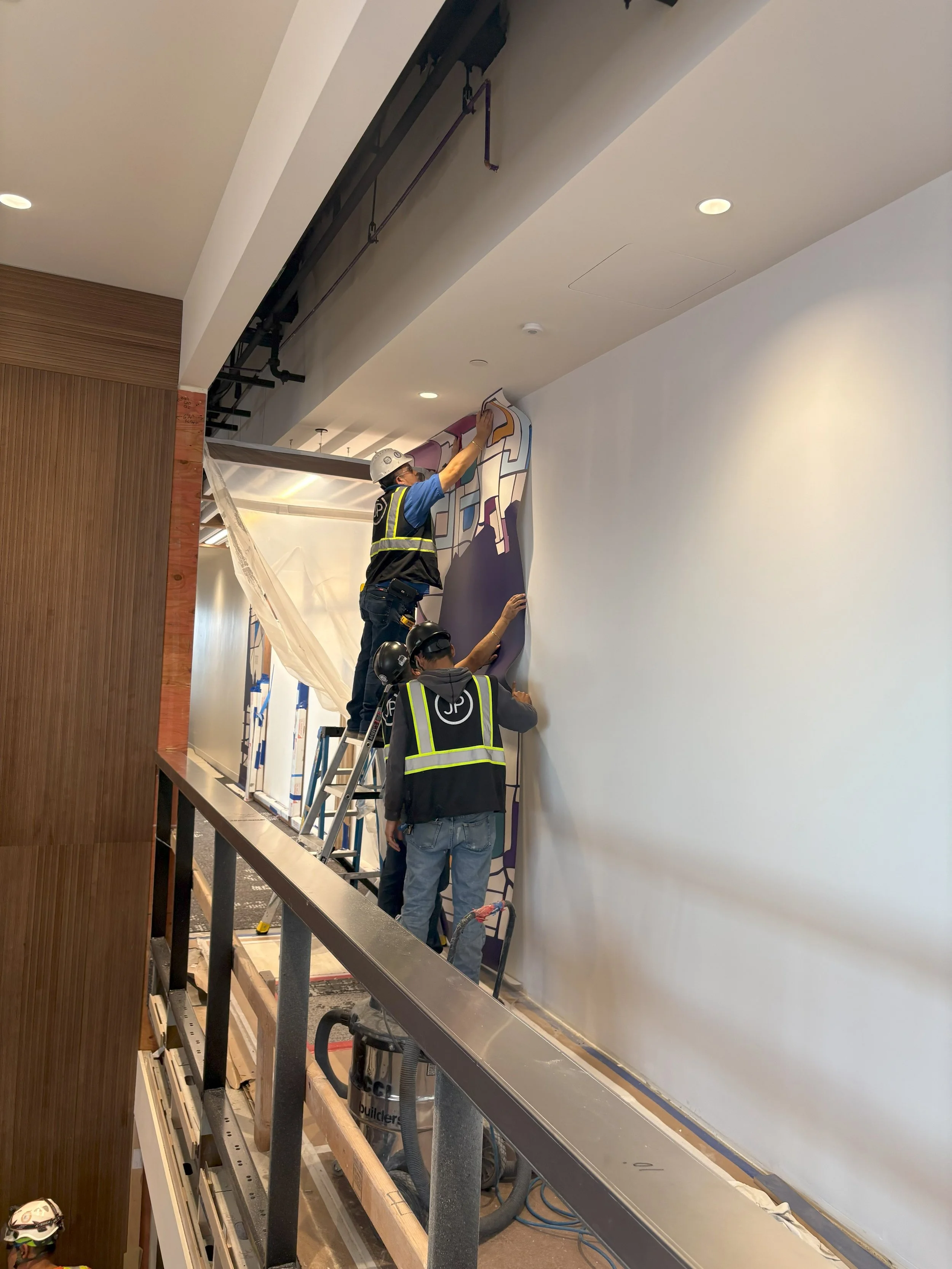 Installer applying custom wallcovering graphics along corridor wall at the KPMG San Jose office.