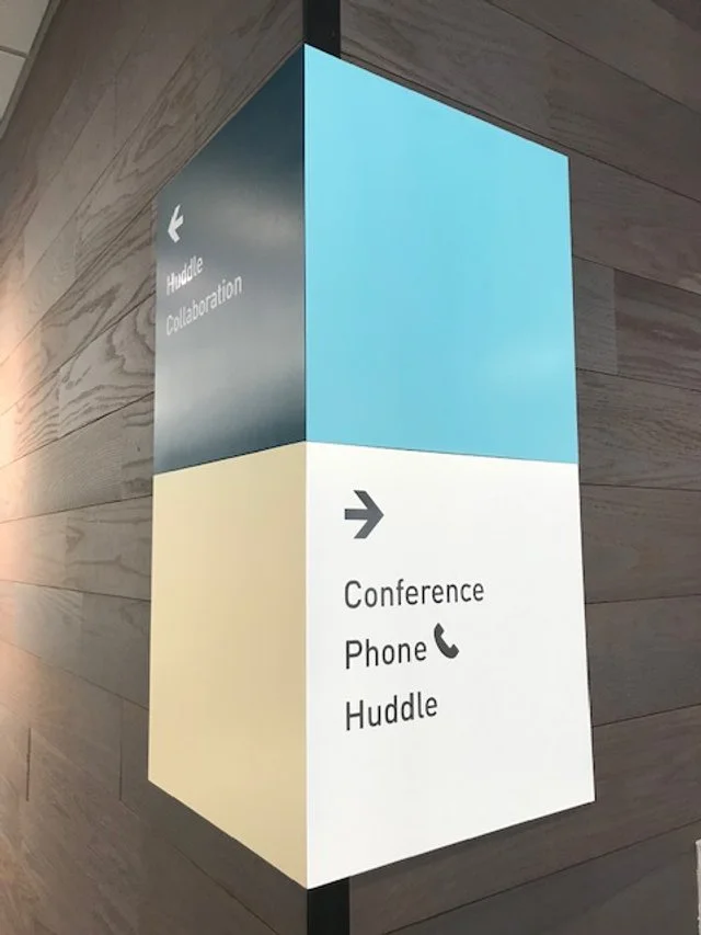 Interior directional wayfinding signage guiding visitors to conference rooms and huddle spaces in corporate office environment