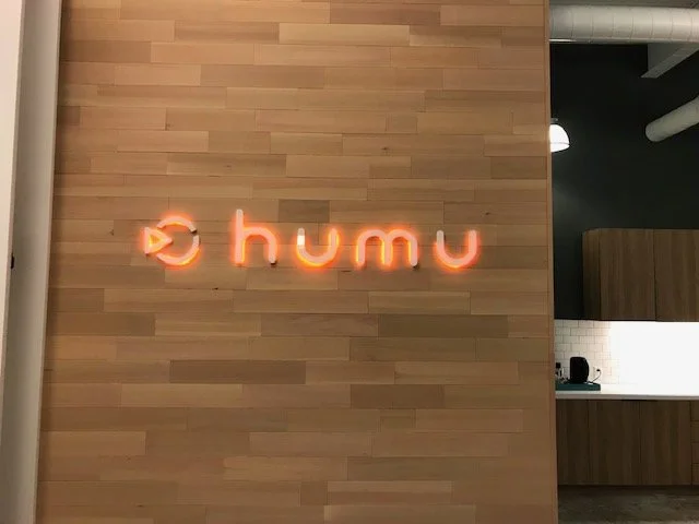 Dimensional Humu lobby logo signage installed on wood feature wall to reinforce brand identity