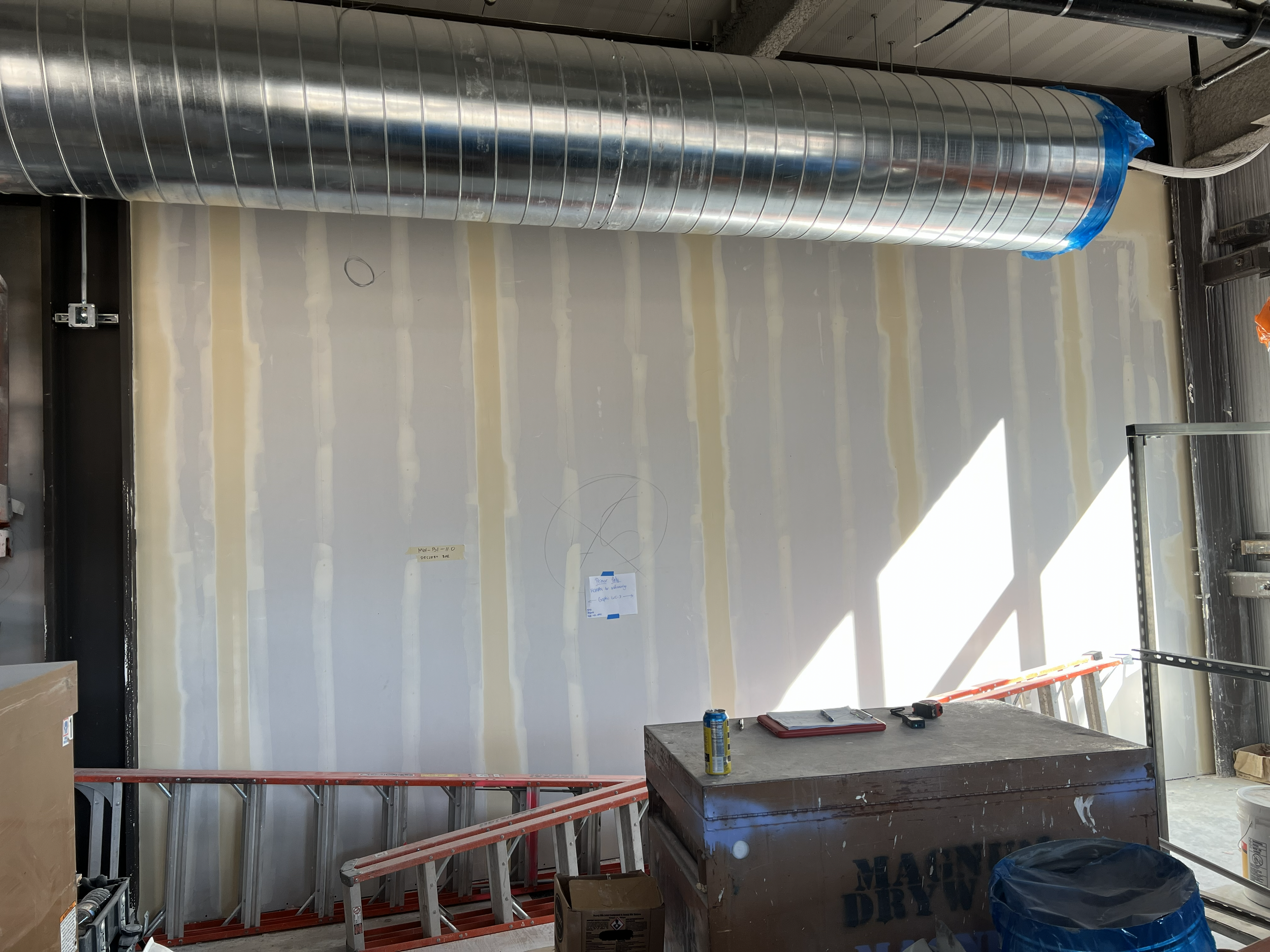 Pre-construction commercial drywall surface preparation for custom wallcovering installation with exposed ductwork and jobsite layout markings