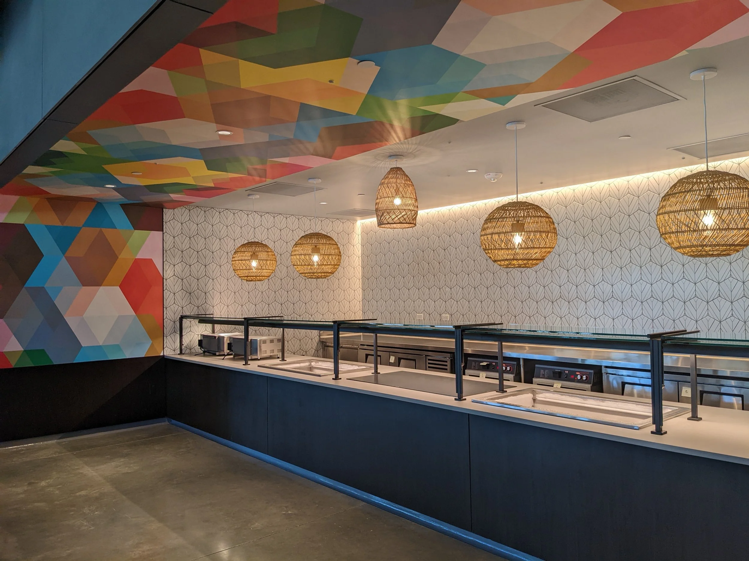 Modern commercial lounge interior featuring geometric mural wallcovering, patterned feature wall, woven pendant lighting, and custom environmental graphics by JP Digital.